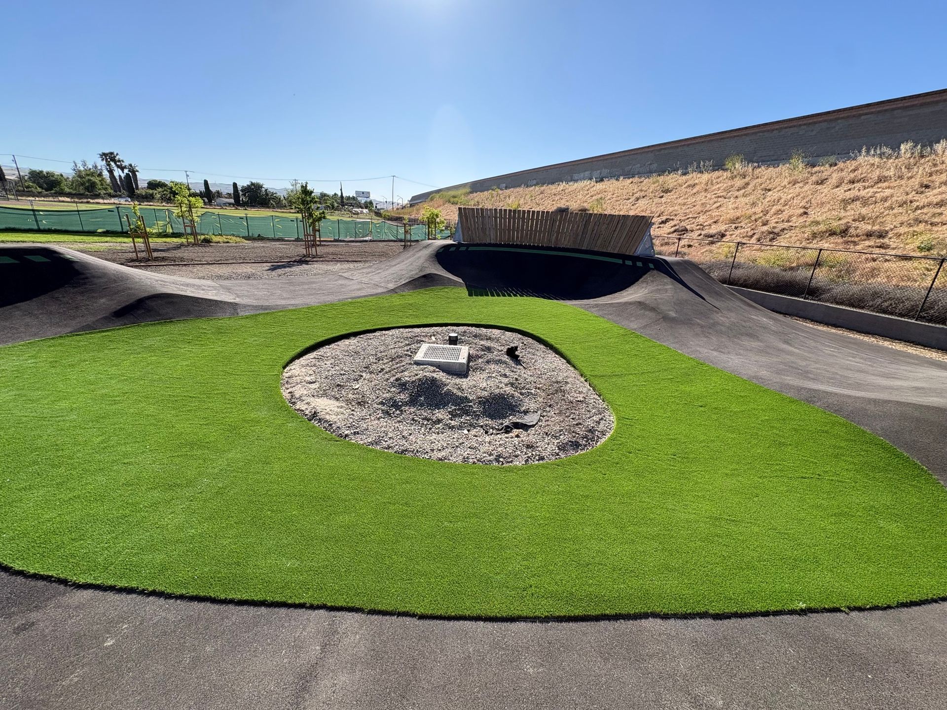 Outdoor mini-golf course with bright green turf, black paths, and a central rock feature under a clear sky