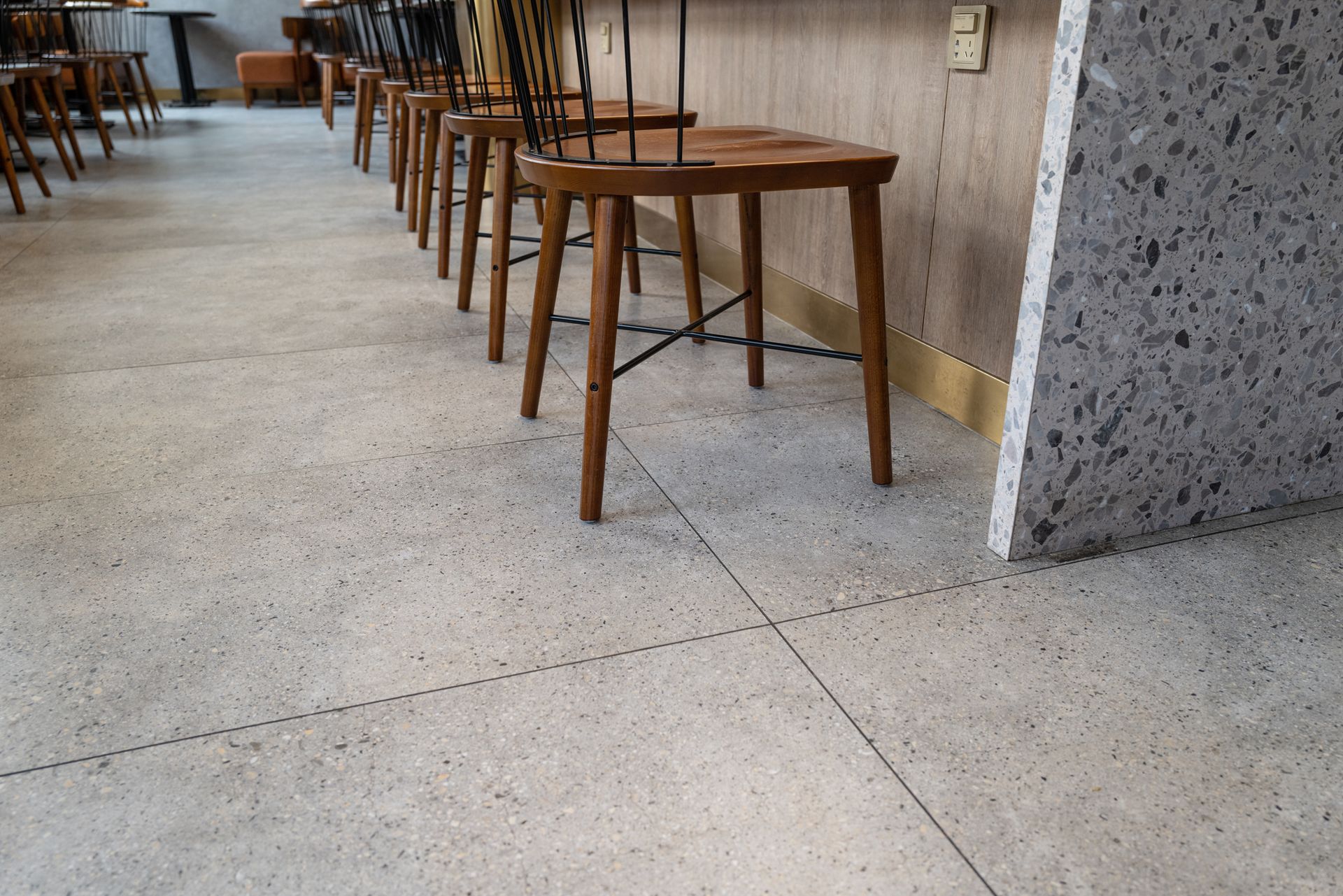 A row of wooden chairs are lined up on a concrete floor in a restaurant.