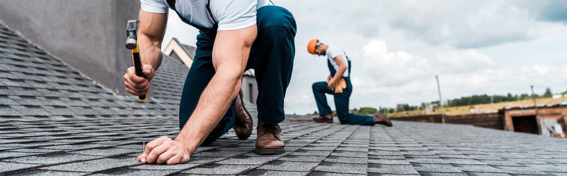 Workers installing shingles on a roof with tools and safety gear.