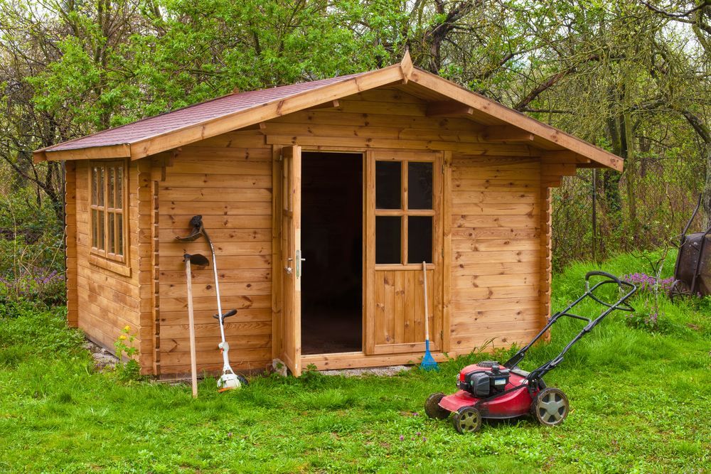 Wooden Shed with Open Door, Lawnmower, and Yard Tools in A Grassy Yard — Complete Sheds In Nowra, NSW
