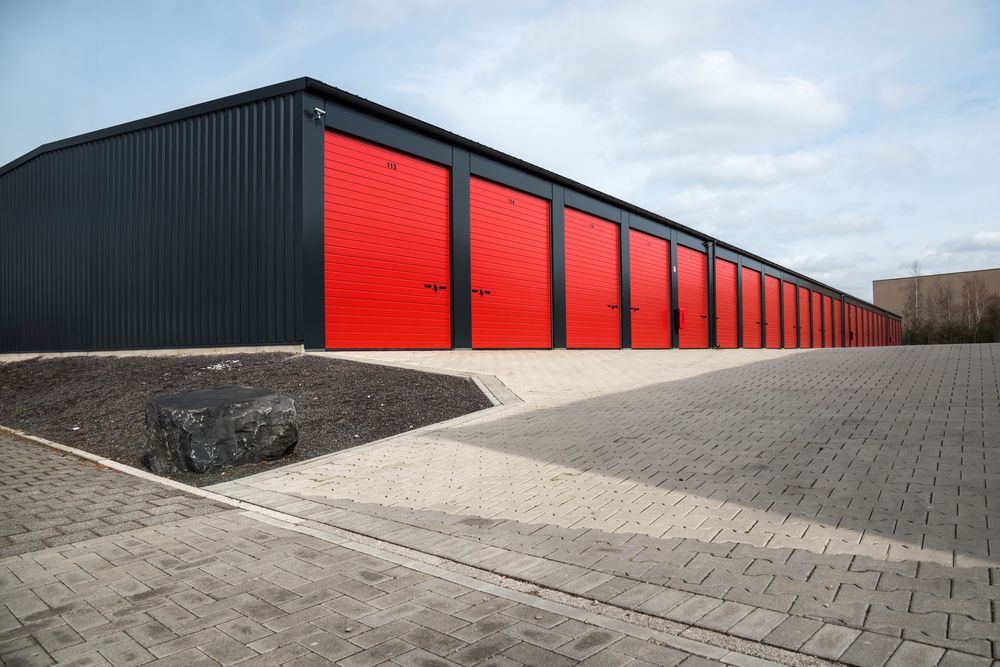 Storage Units with Red Doors and Black Siding, Outdoors on A Paved Lot — Complete Sheds In Bowral, NSW