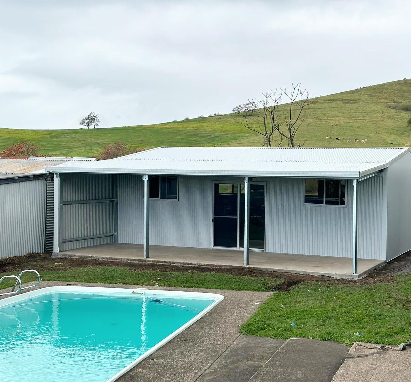 White Building with A Pool, Green Grass, and Rolling Hills — Complete Sheds In Marulan, NSW