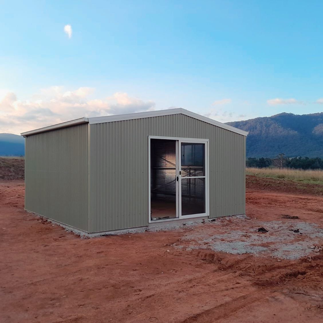 Green Metal Shed on A Red Dirt Lot with Sliding Glass Door — Complete Sheds In Marulan, NSW