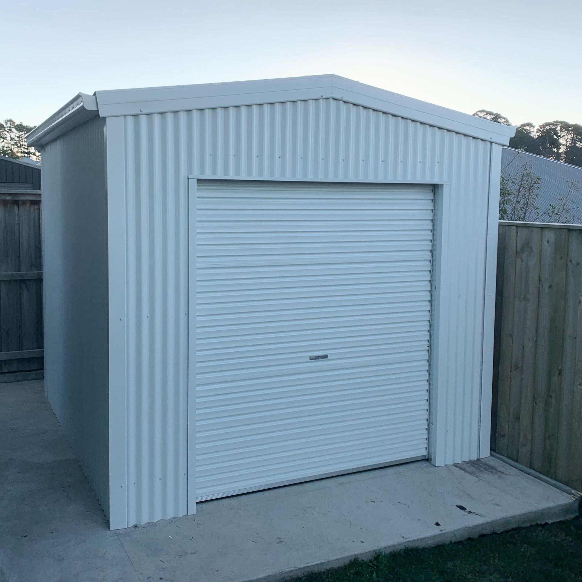 White Corrugated Metal Shed with Closed Garage Door on A Concrete Pad — Complete Sheds In Marulan, NSW