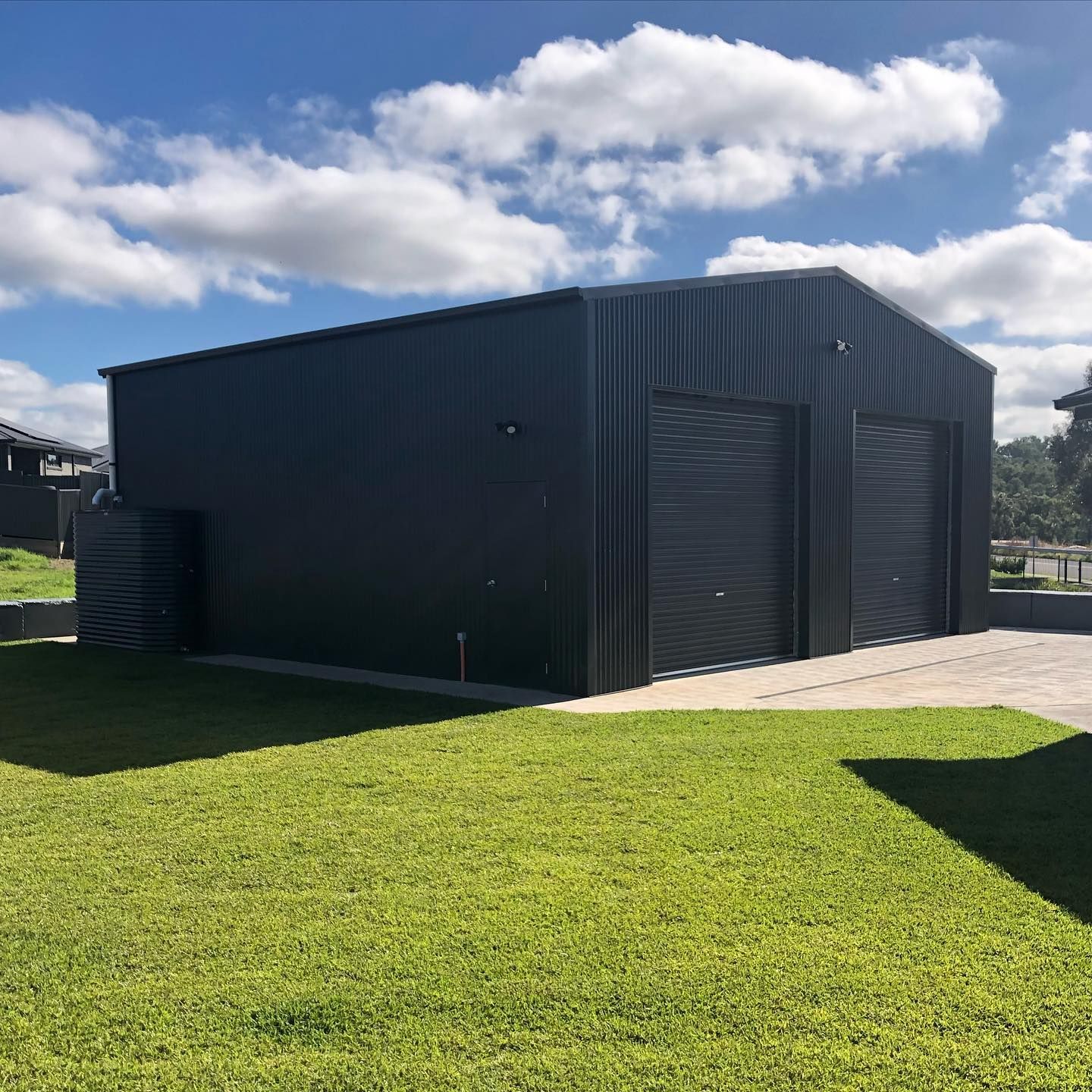 Dark Grey Shed with Two Roller Doors, on Green Grass, Under a Cloudy Sky — Complete Sheds In Marulan, NSW