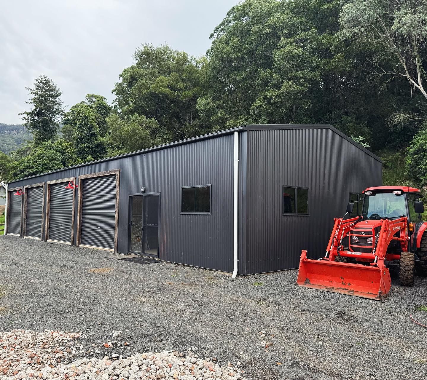 Black Garage Building with Three Doors, a Side Entrance, and Rocks — Complete Sheds In Marulan, NSW