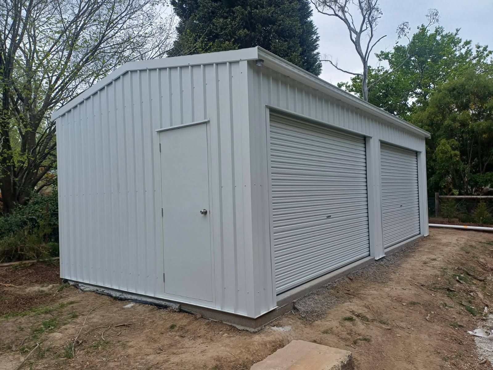 White metal shed with a door and two roll-up garage doors. Located outdoors.