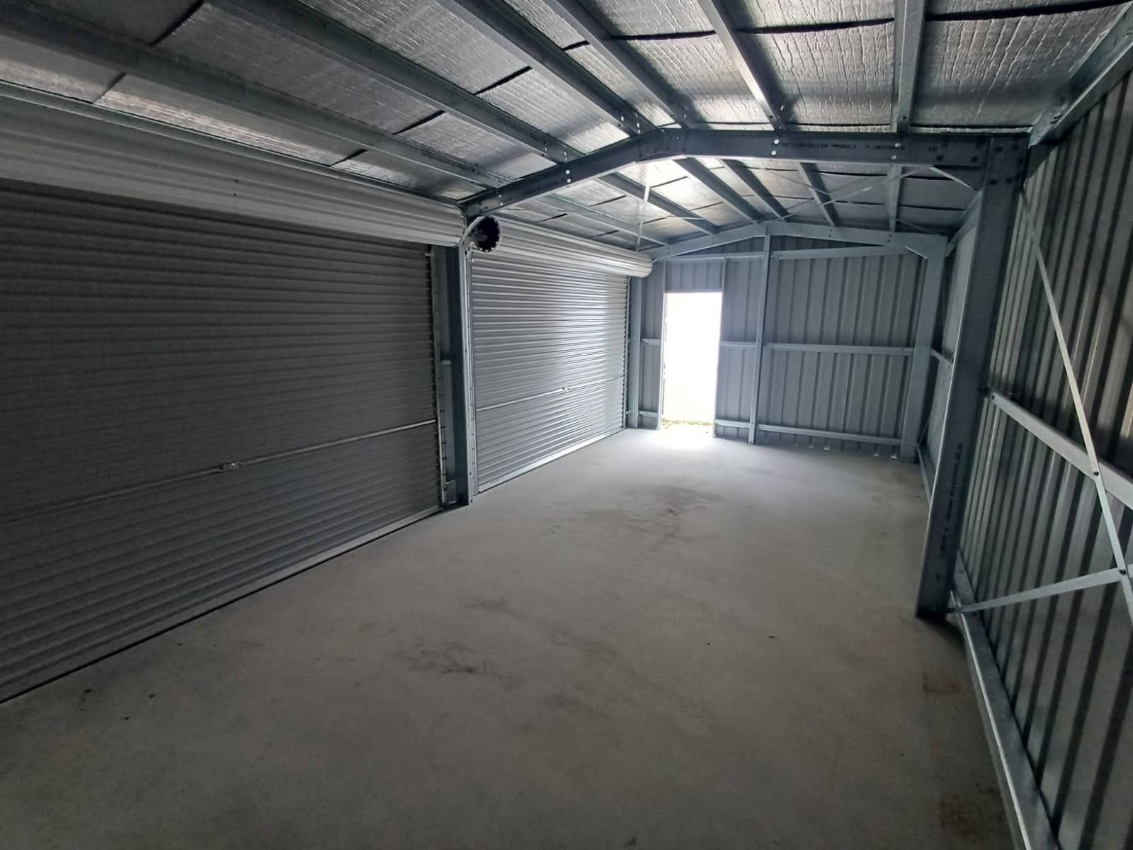 Interior of a metal shed with a roller door and an open doorway.