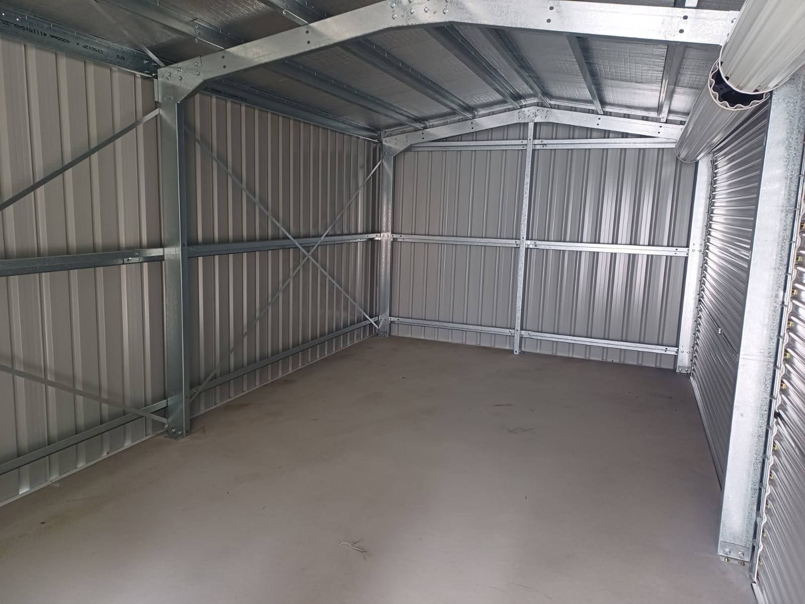 Empty metal shed interior with concrete floor, metal walls, and roof structure.