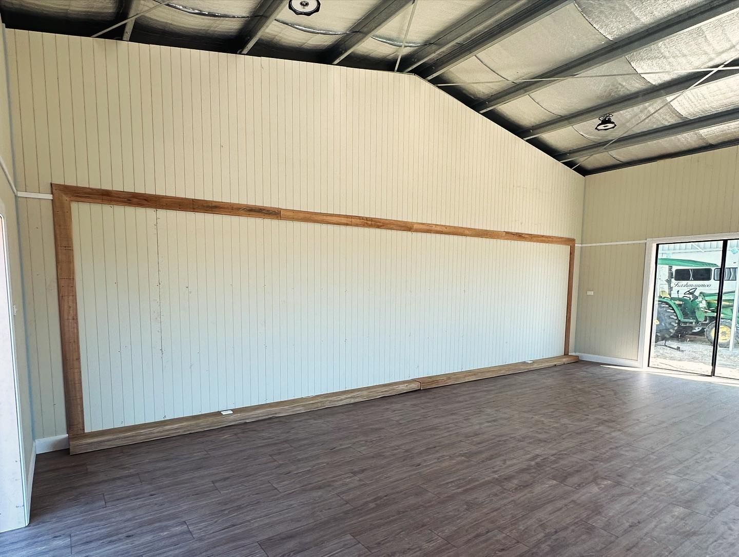 Interior of a light-coloured building with wood-look flooring and a framed wall.