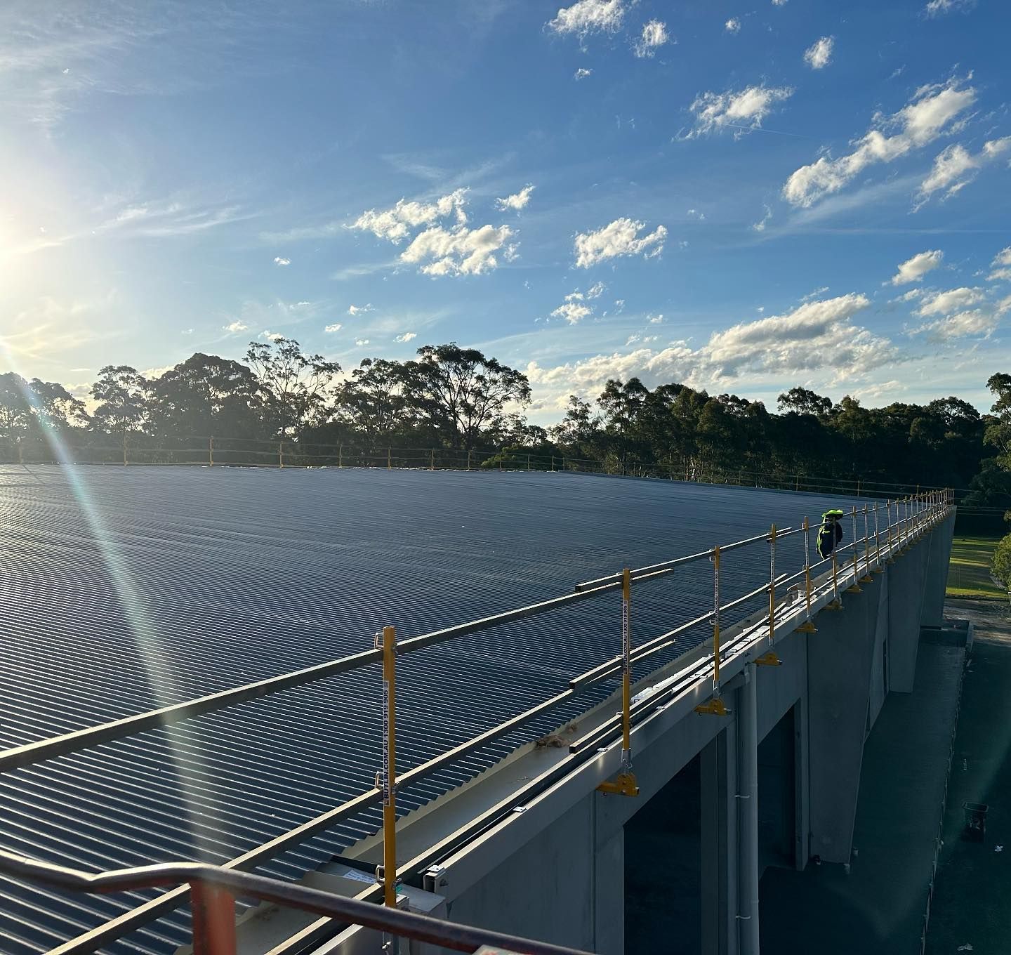 Rooftop with metal roofing and safety rails against a bright sky with trees in the distance.