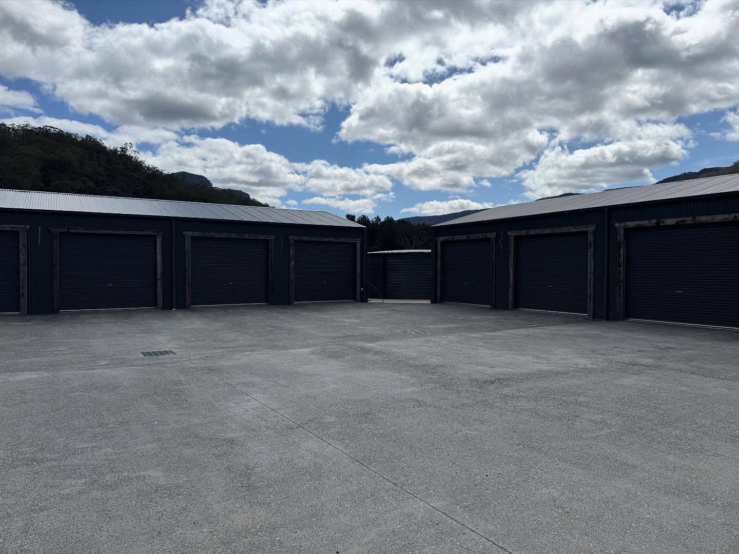 Storage units with dark blue doors and roofs, in front of a gravel lot, under a cloudy sky.