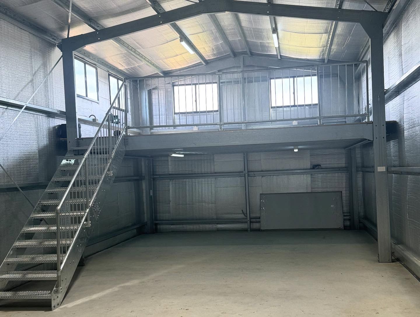 Interior of a metal industrial building with a mezzanine level and a staircase. Walls are grey.