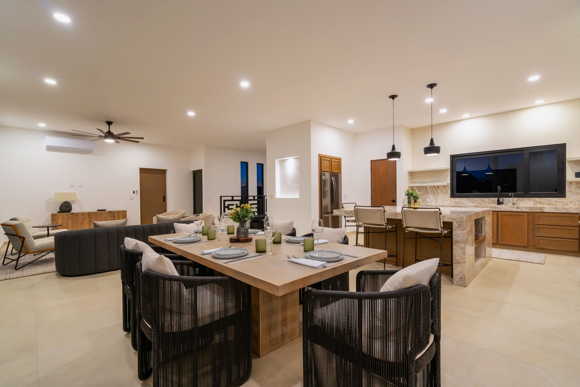 Open-concept dining and kitchen area with dining table and island seating. Neutral tones, modern decor.
