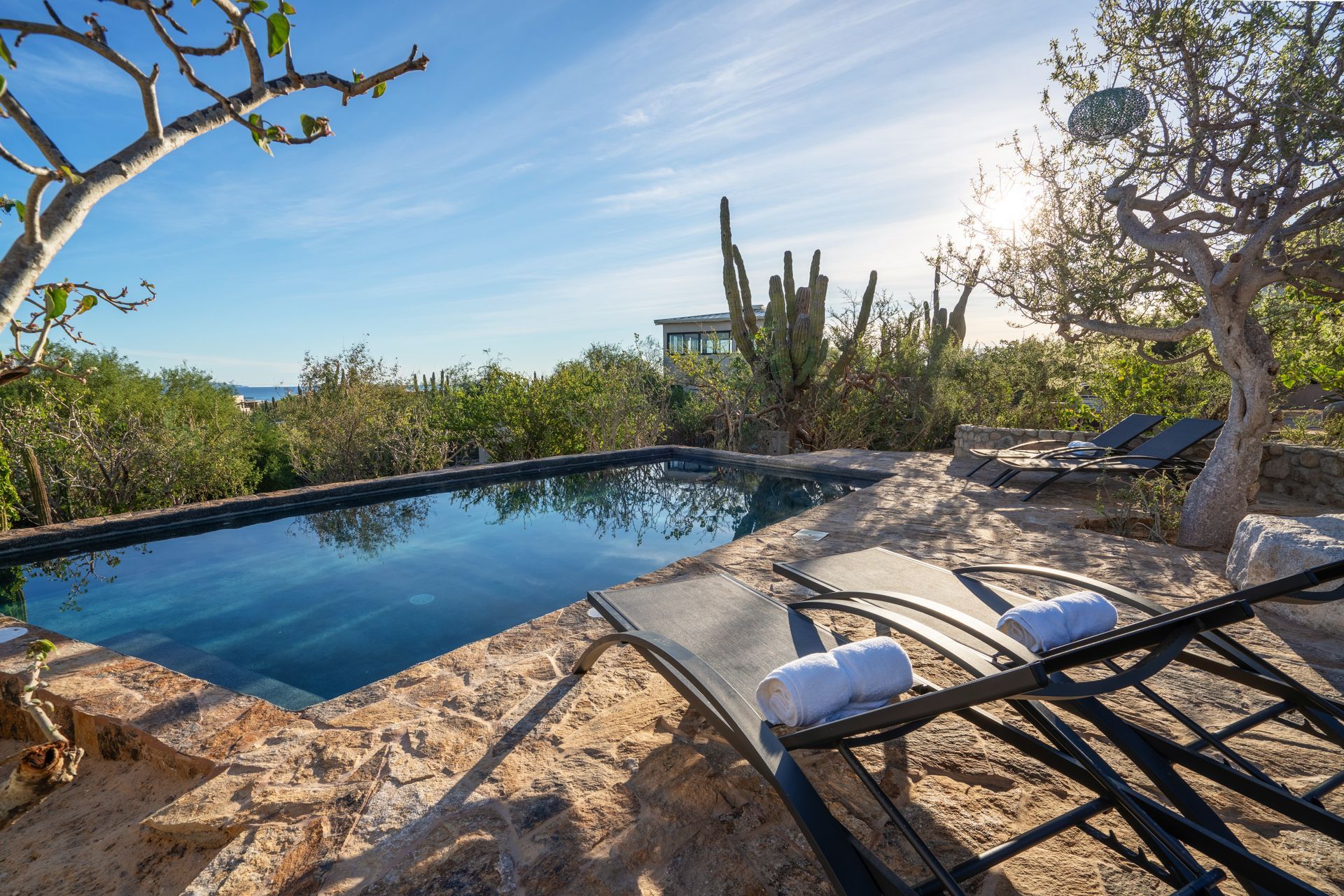 Pool with lounge chairs overlooking a desert landscape under a sunny sky.