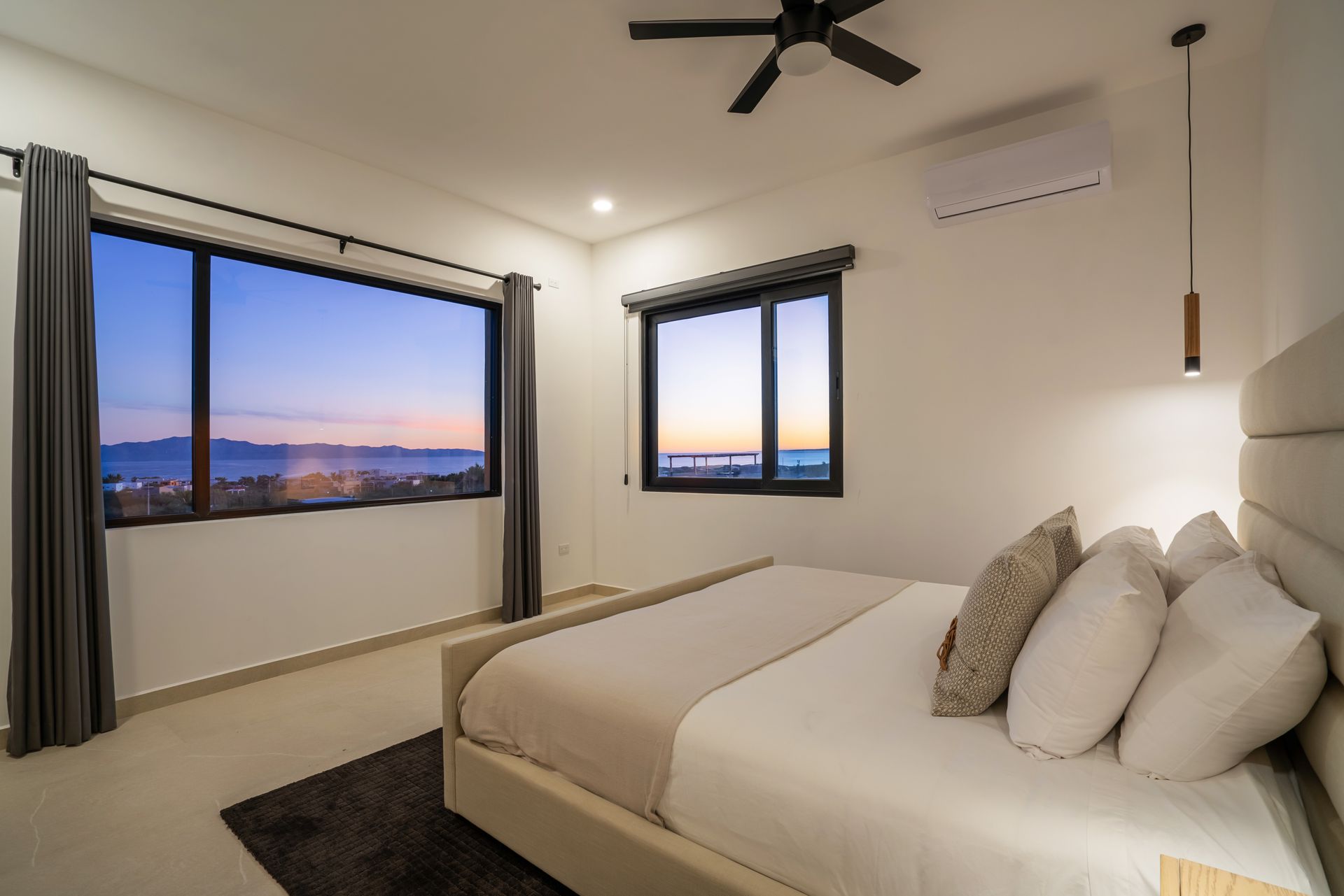 Bedroom with bed, pillows, window with twilight view, gray curtains, and ceiling fan.