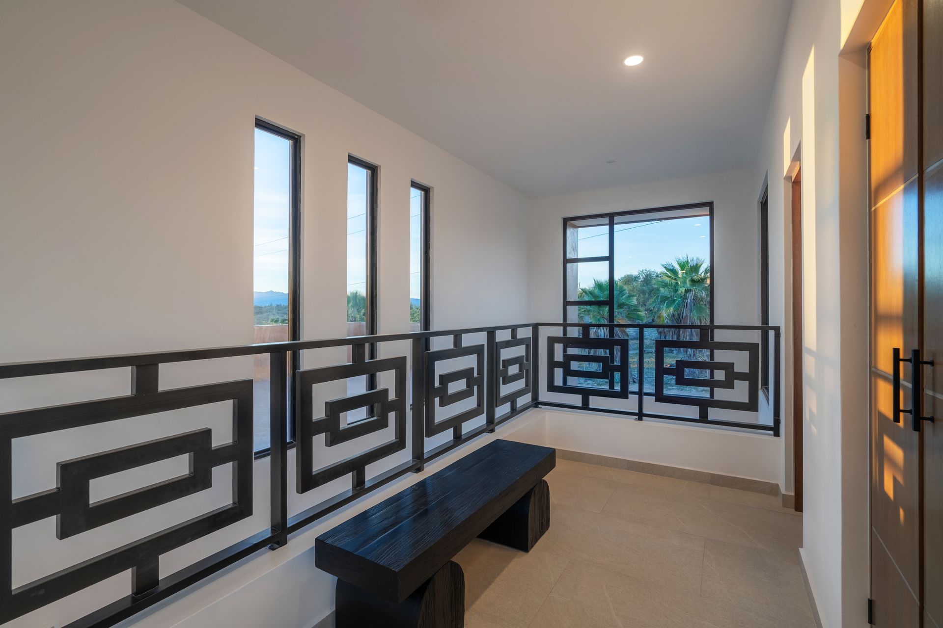 Hallway with black geometric railing, small bench, and windows with outdoor view.