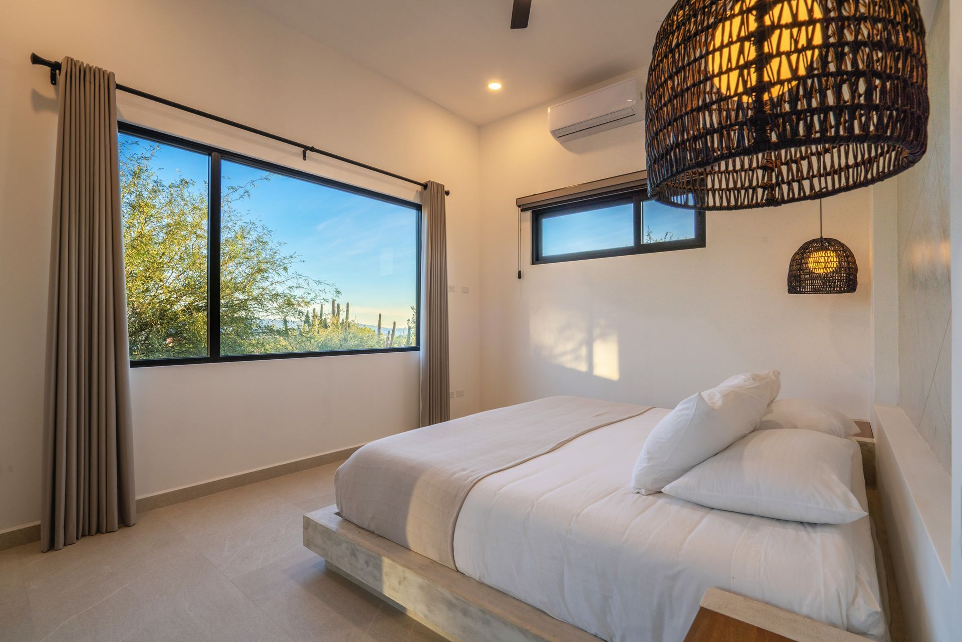 Bedroom with a large window overlooking trees, a bed, and a decorative hanging light fixture.