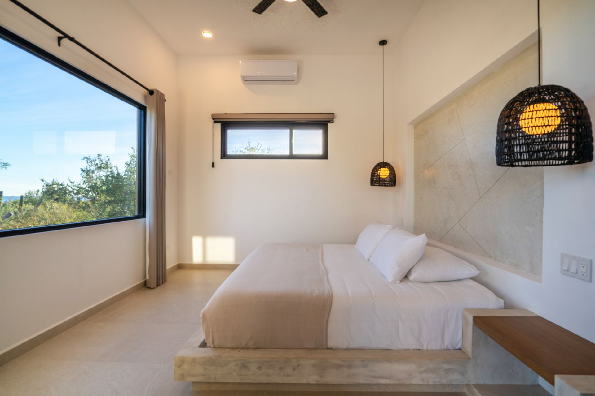 Bedroom with bed, large window, neutral colors, and decorative lamp.