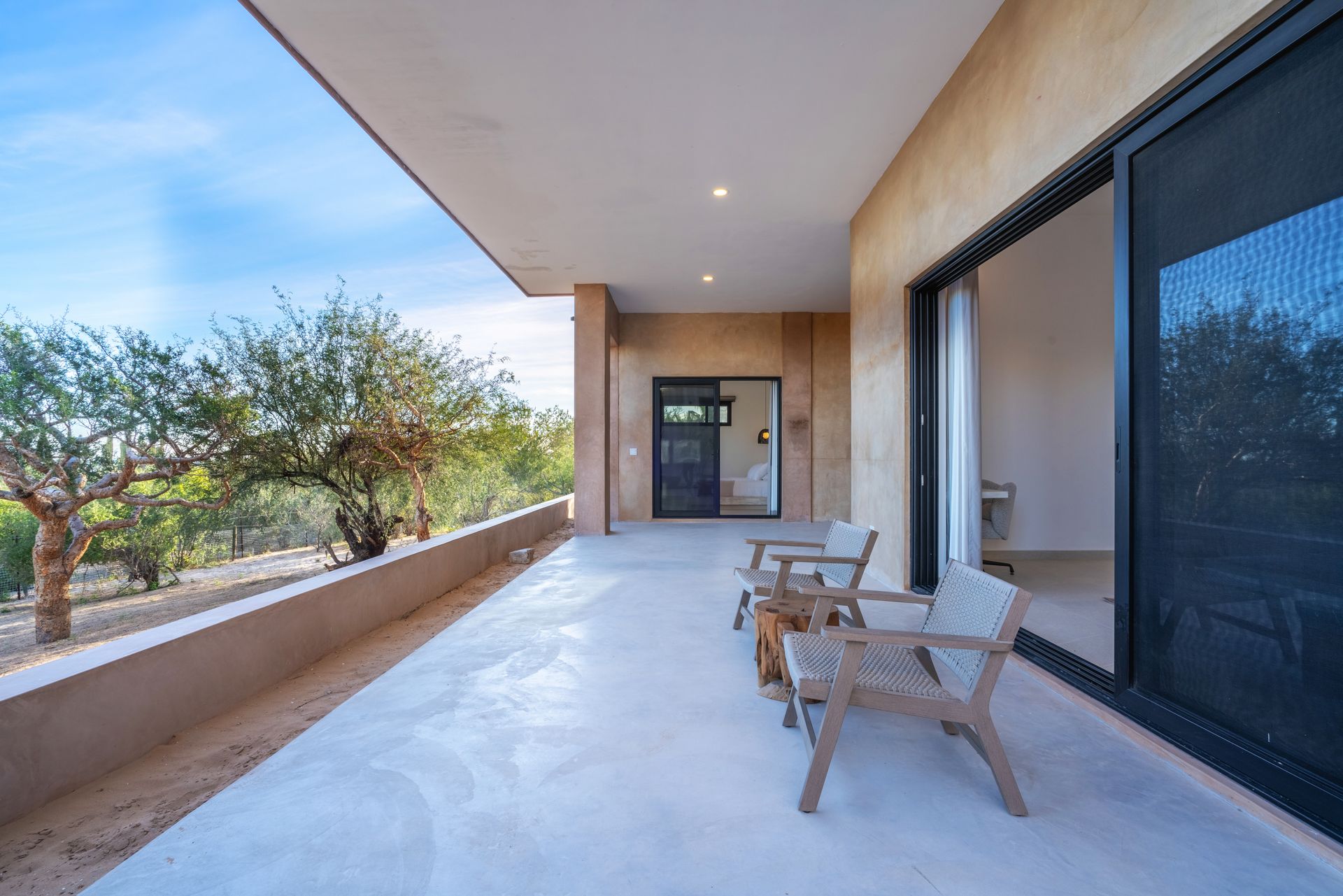 Outdoor patio with seating, overlooking trees and a blue sky. A sliding glass door and entrance door are visible.