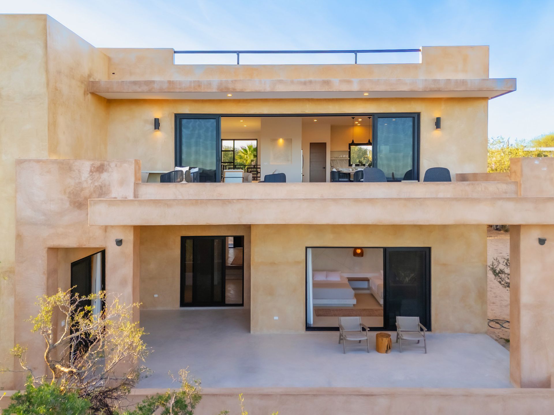 Two-story adobe-style building with open patios. Sliding glass doors reveal living spaces.