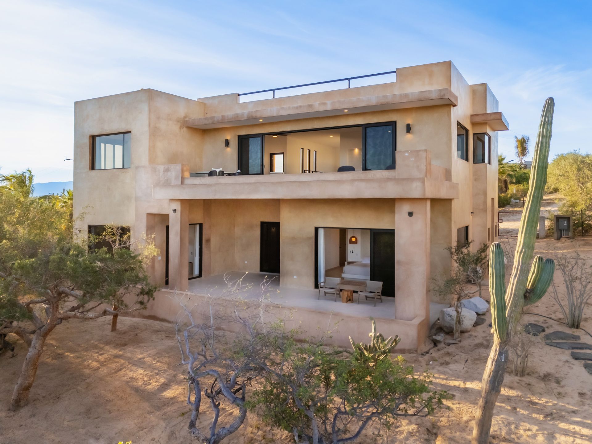 Two-story beige stucco house with open balconies and desert landscaping.