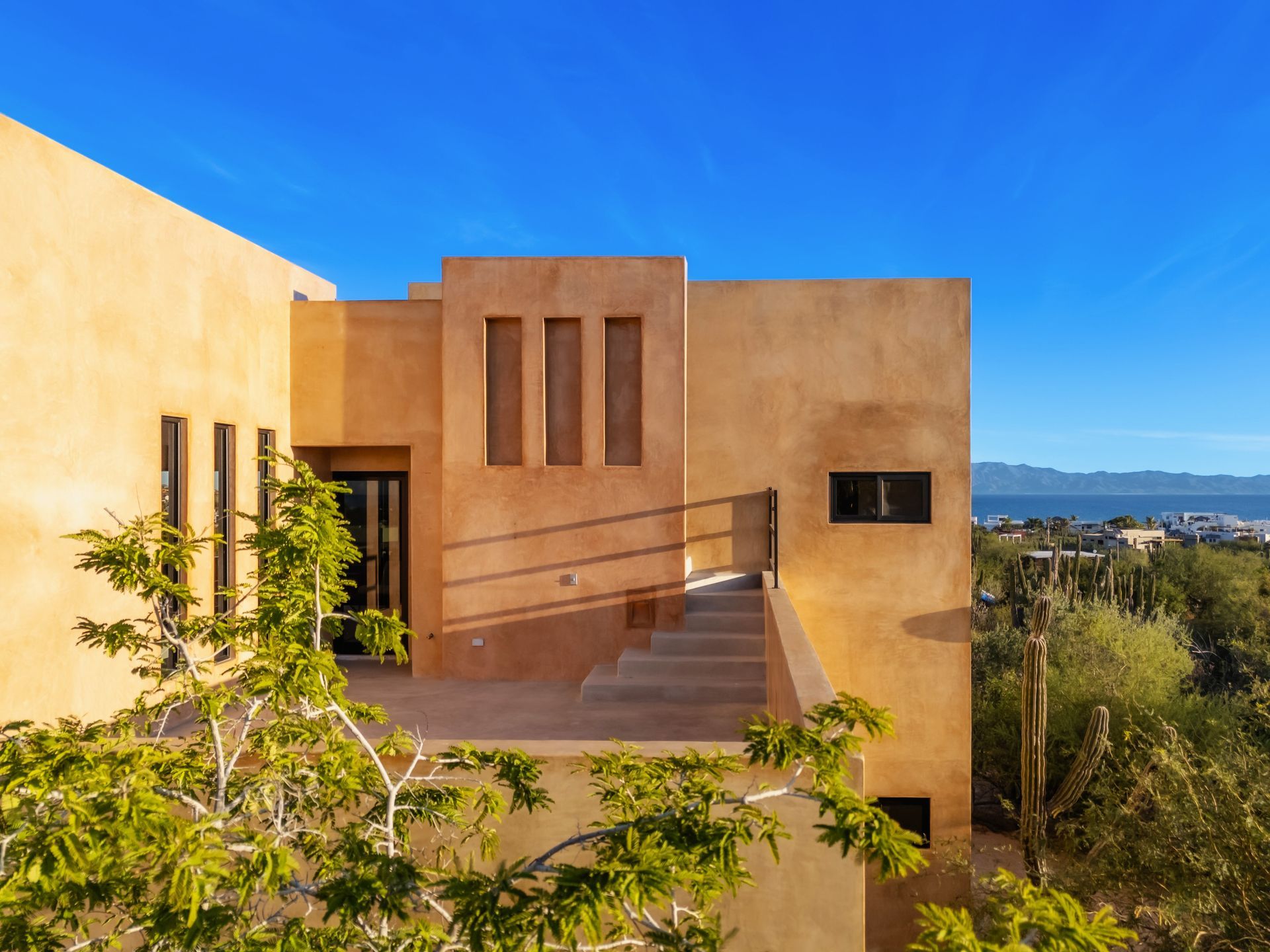 Beige stucco building with rooftop terrace, blue sky, and desert landscape.