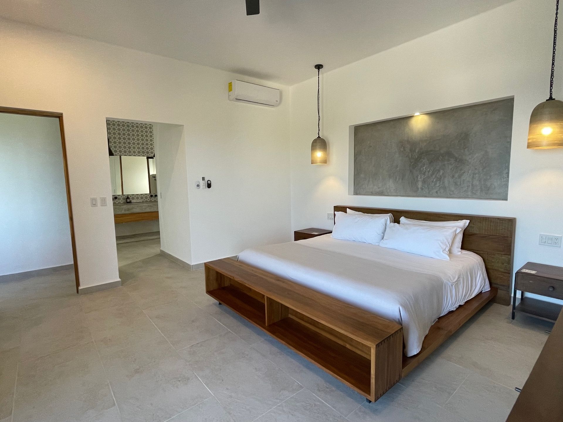 Bedroom with wooden bed, nightstands, and concrete wall accent. Open doorway to kitchen.