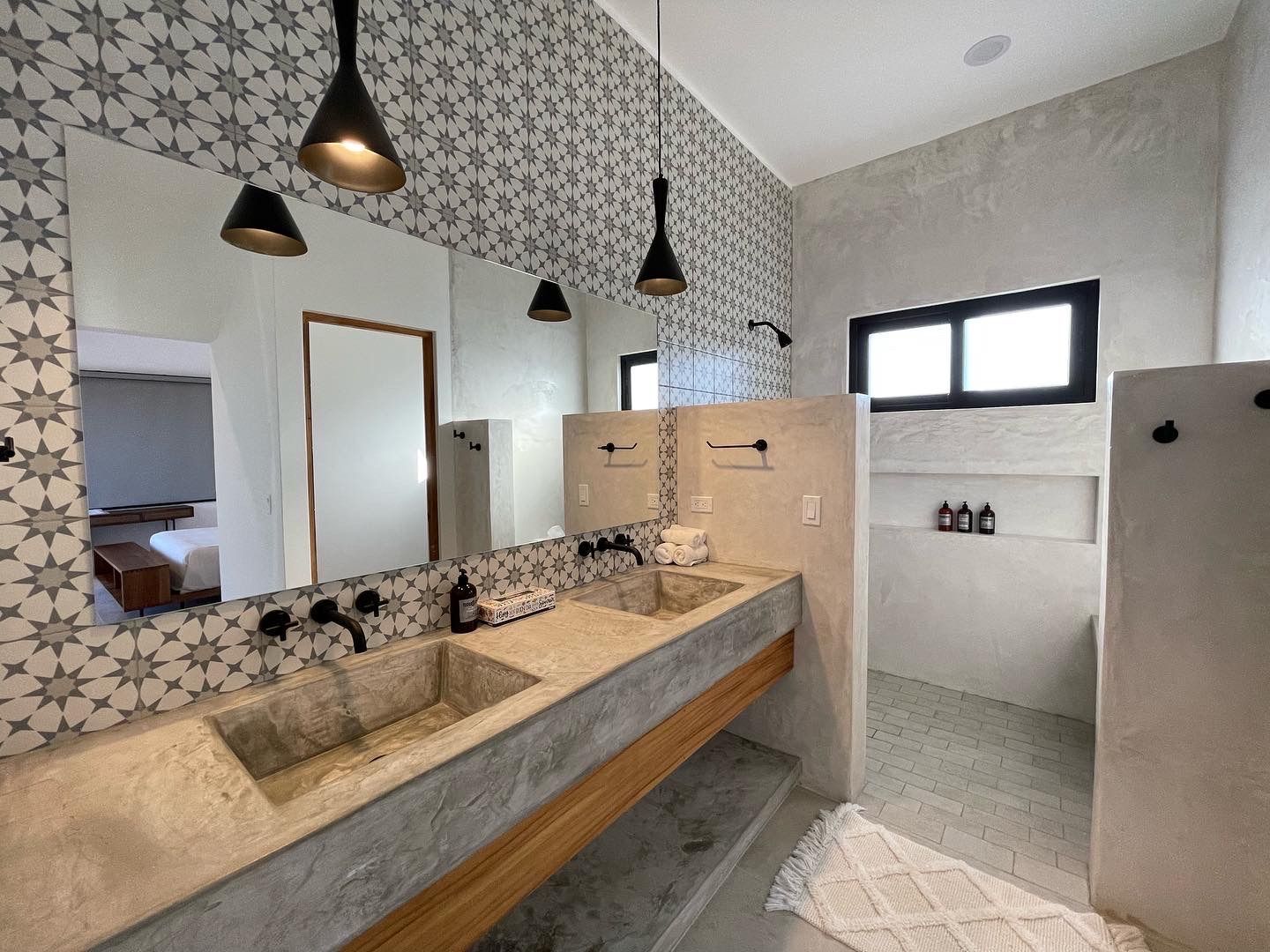Modern bathroom with patterned wall, double sinks, large mirrors, and shower area.