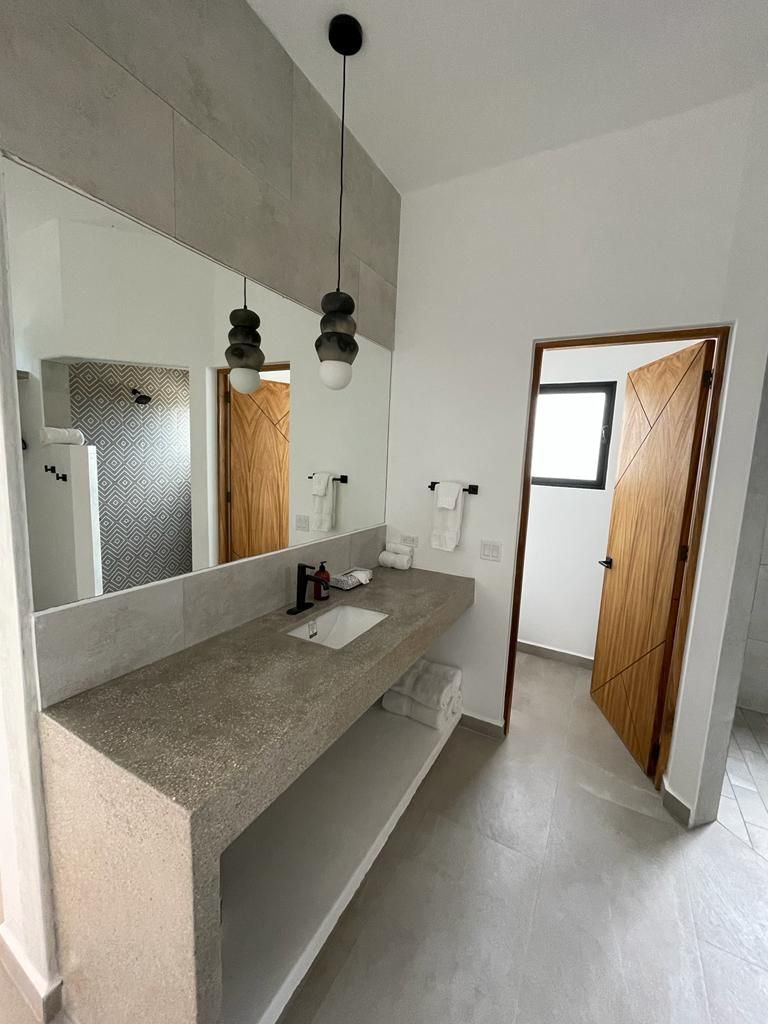 Bathroom with a long gray countertop, large mirror, and open wooden doors. Two pendant lights hang above the sink.