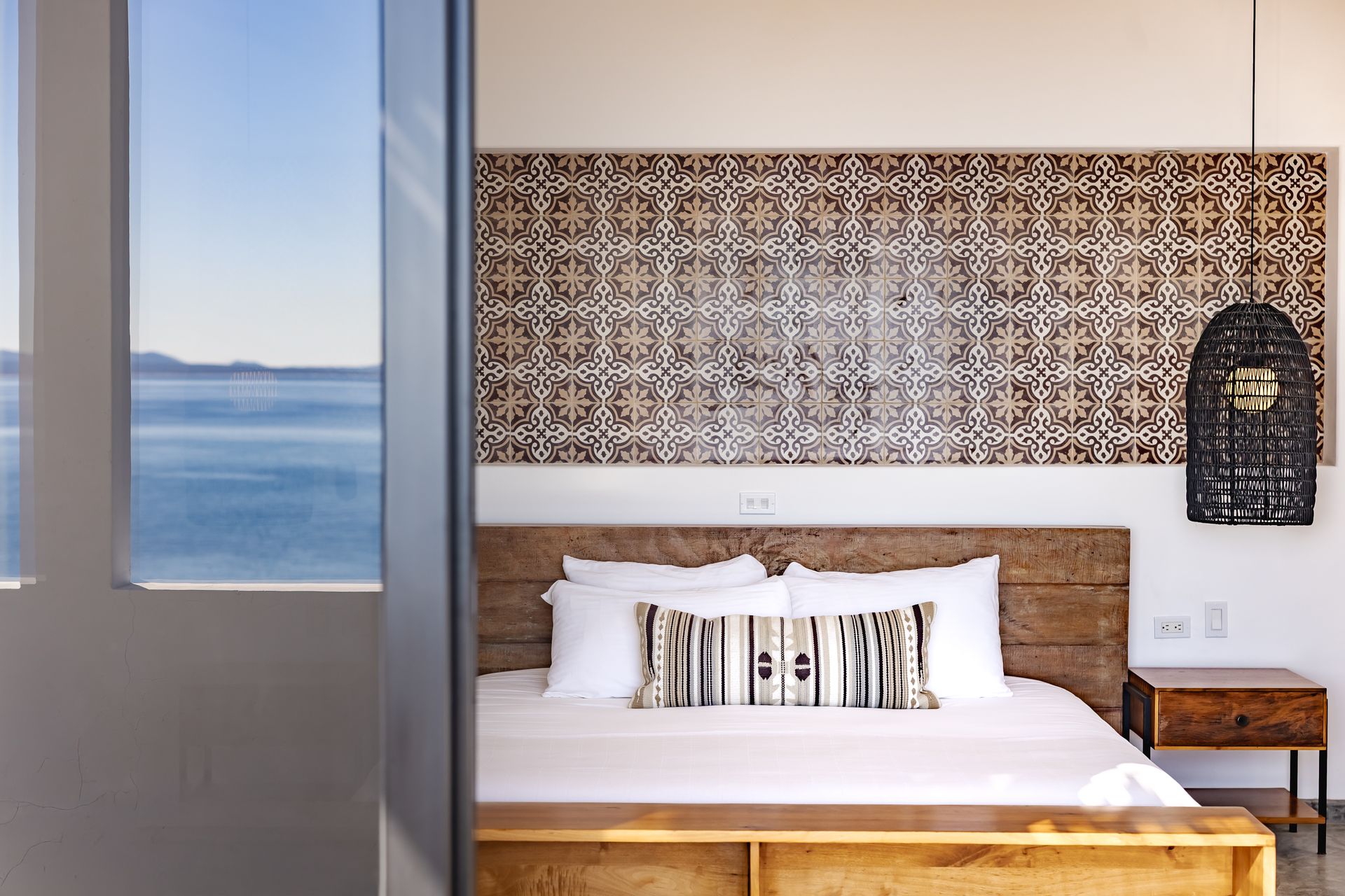 Bedroom with ocean view, wooden bed frame, patterned headboard, hanging light, and nightstand.