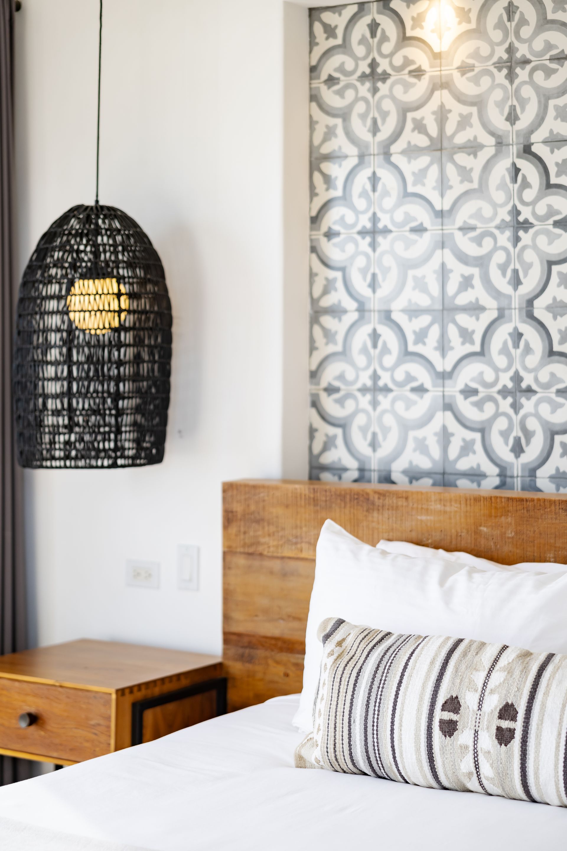 Bedroom with a wooden headboard, patterned wall tiles, a woven pendant light, and a nightstand.