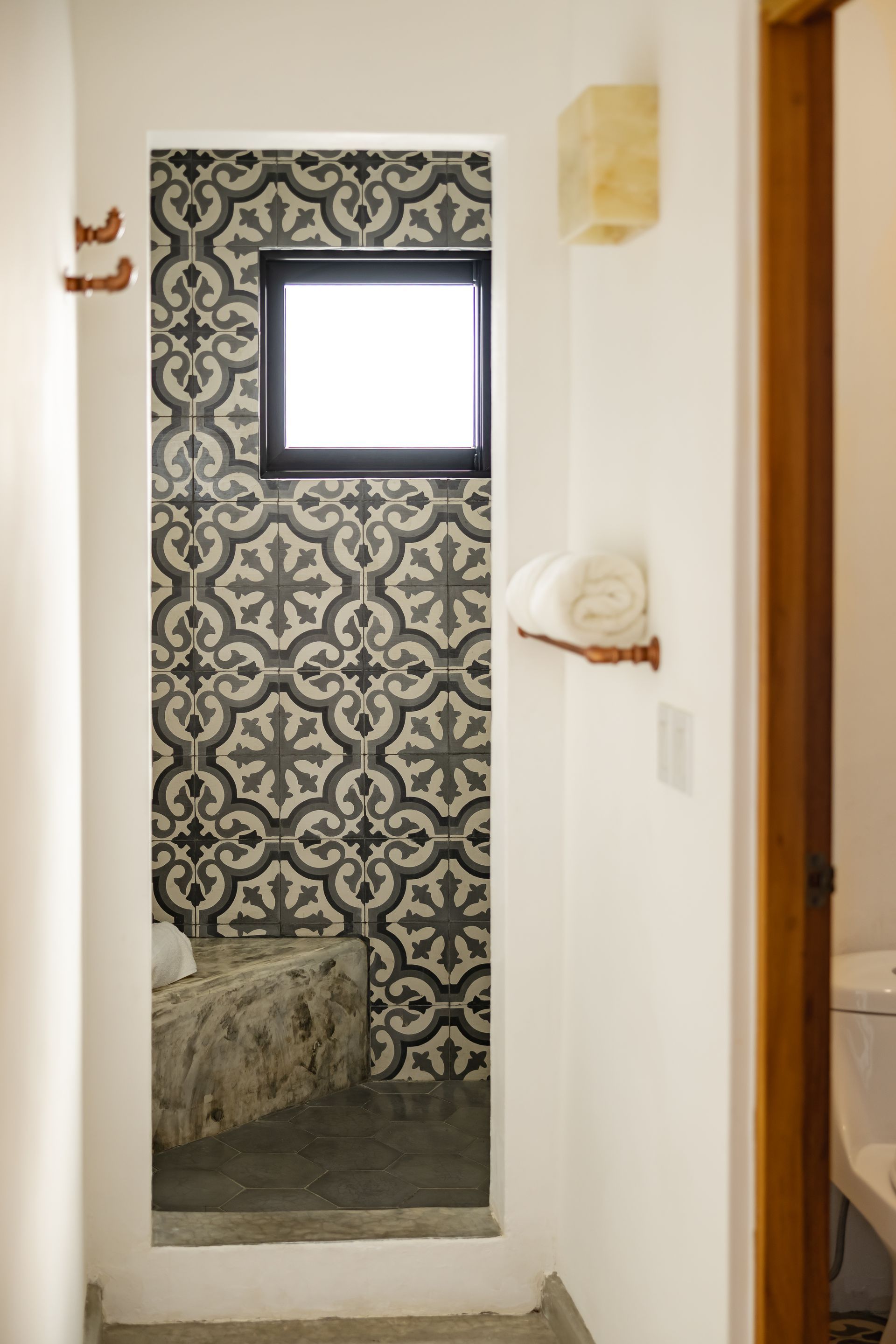 Narrow hallway with patterned tile shower entrance, towels, and a window.