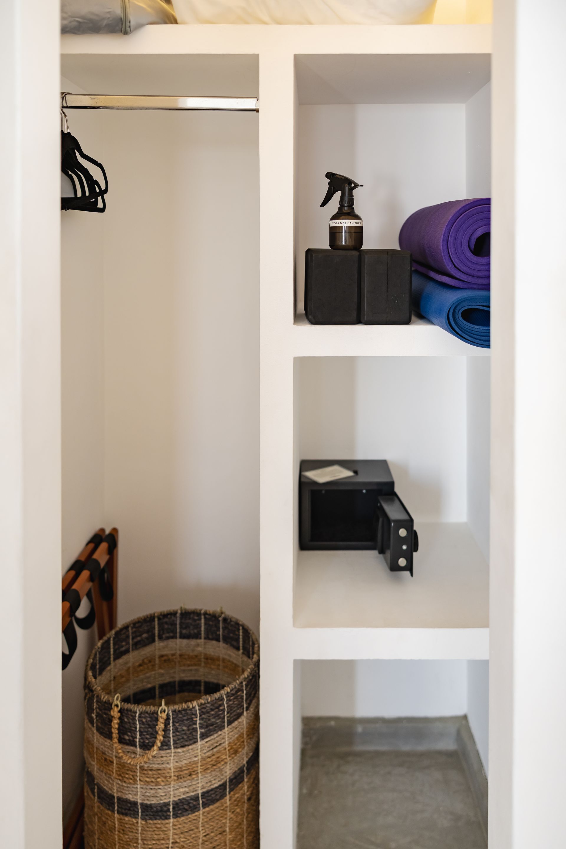 White built-in closet with shelves and rod. Contains yoga mats, spray bottle, blocks, and a woven basket.