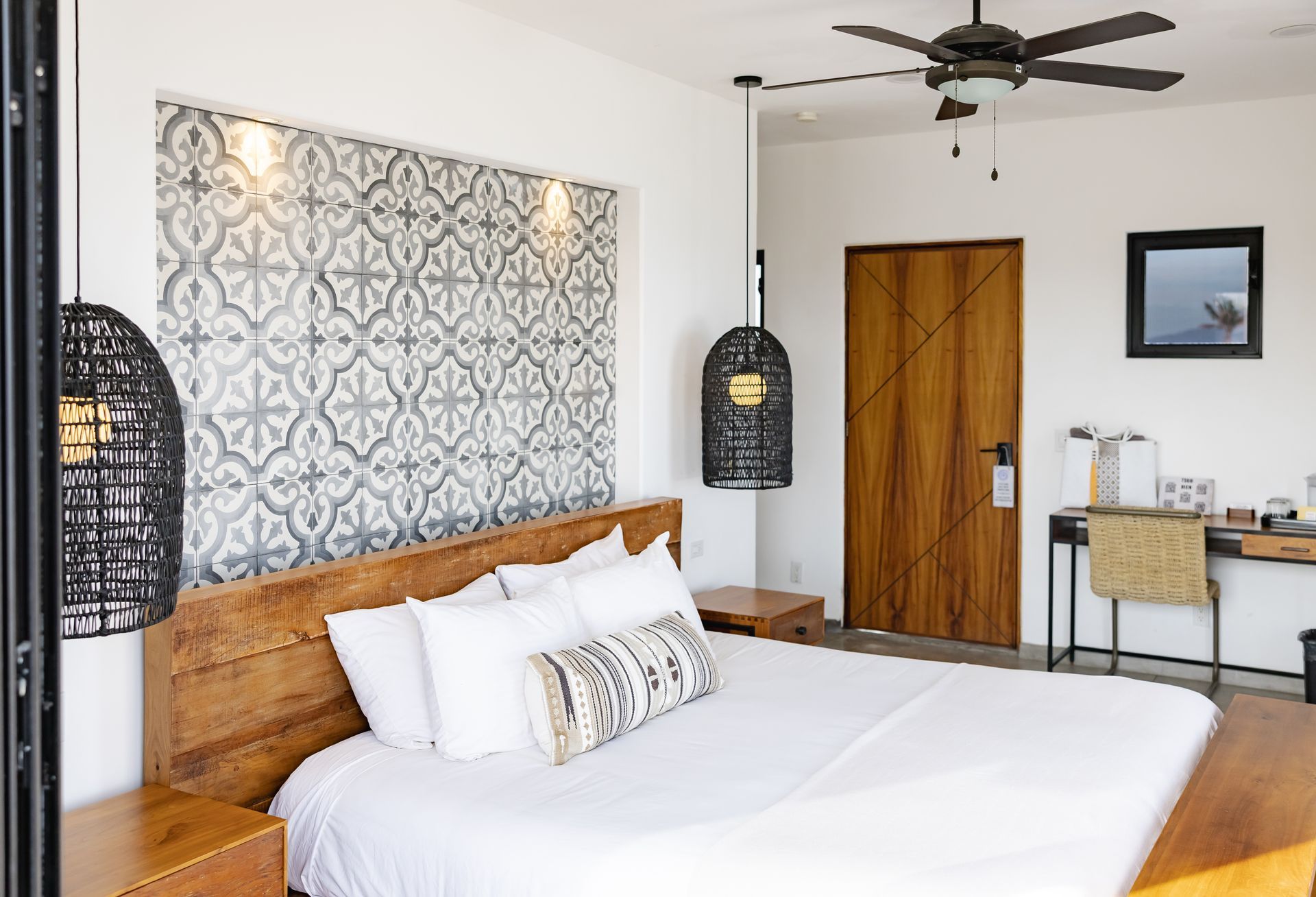 Bedroom with wood bed frame, patterned accent wall, dark pendant lights, desk, and ceiling fan.