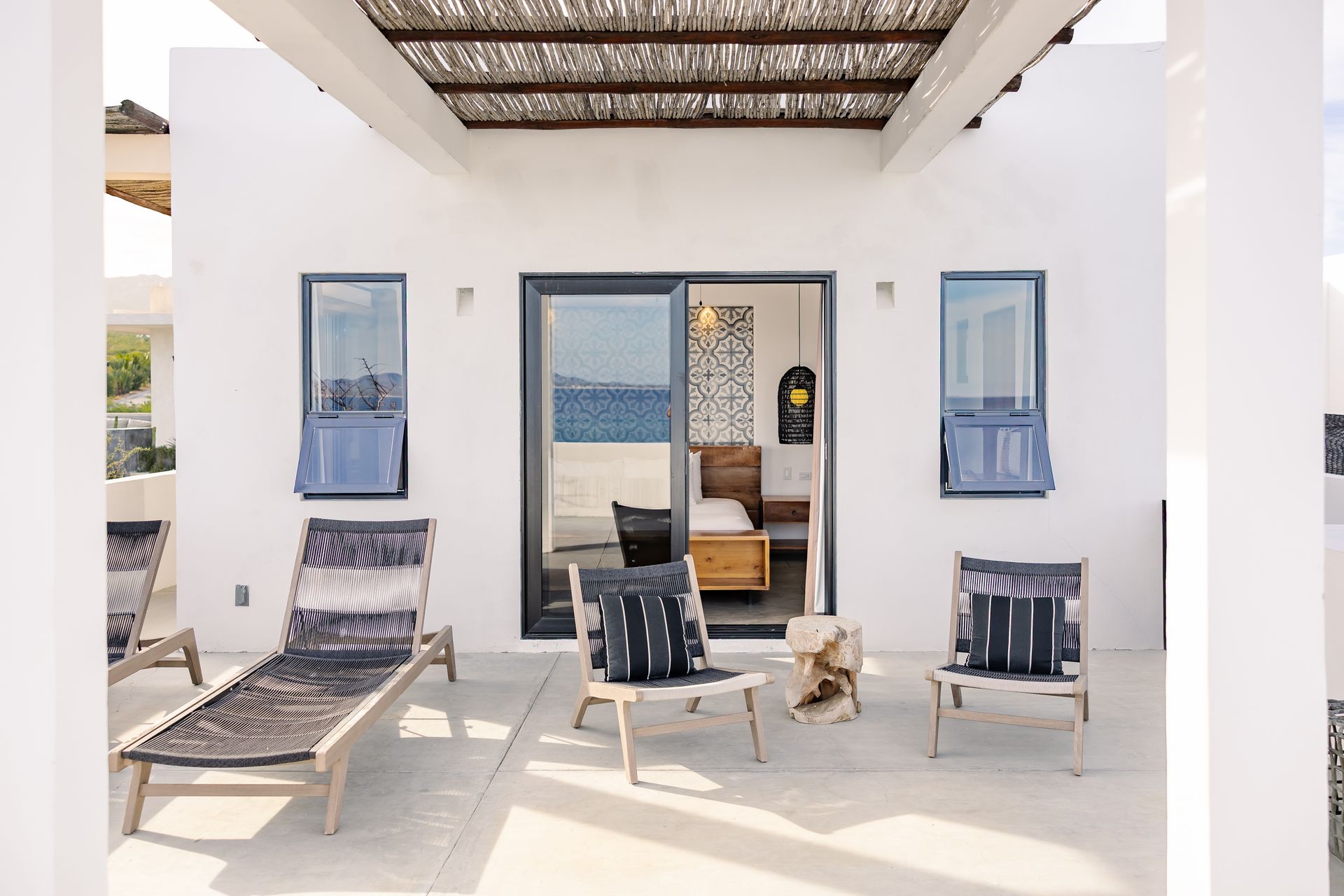 Patio with lounge chairs, open door to bedroom, white walls, and ocean view.
