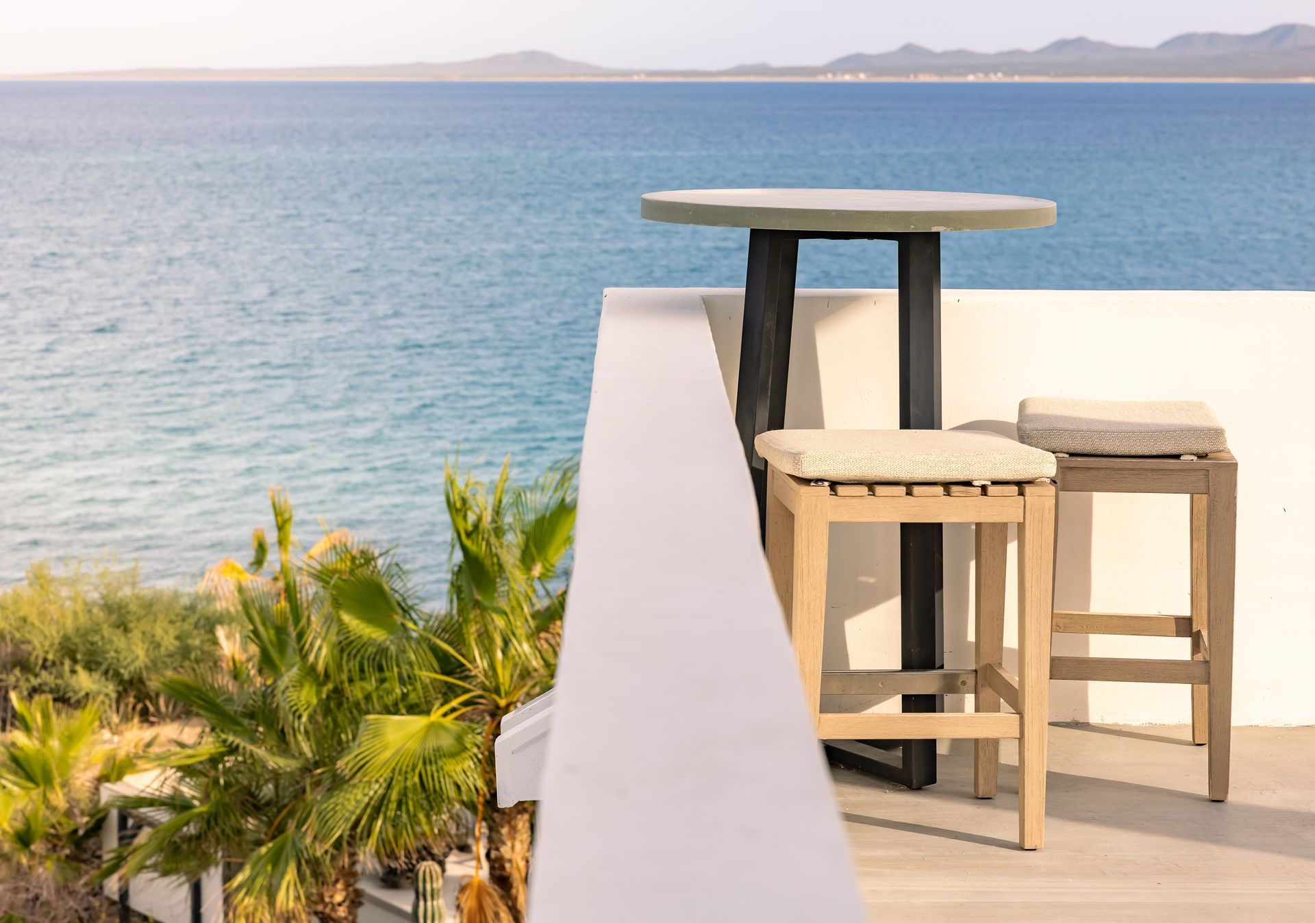 Balcony with table and stools overlooking ocean.