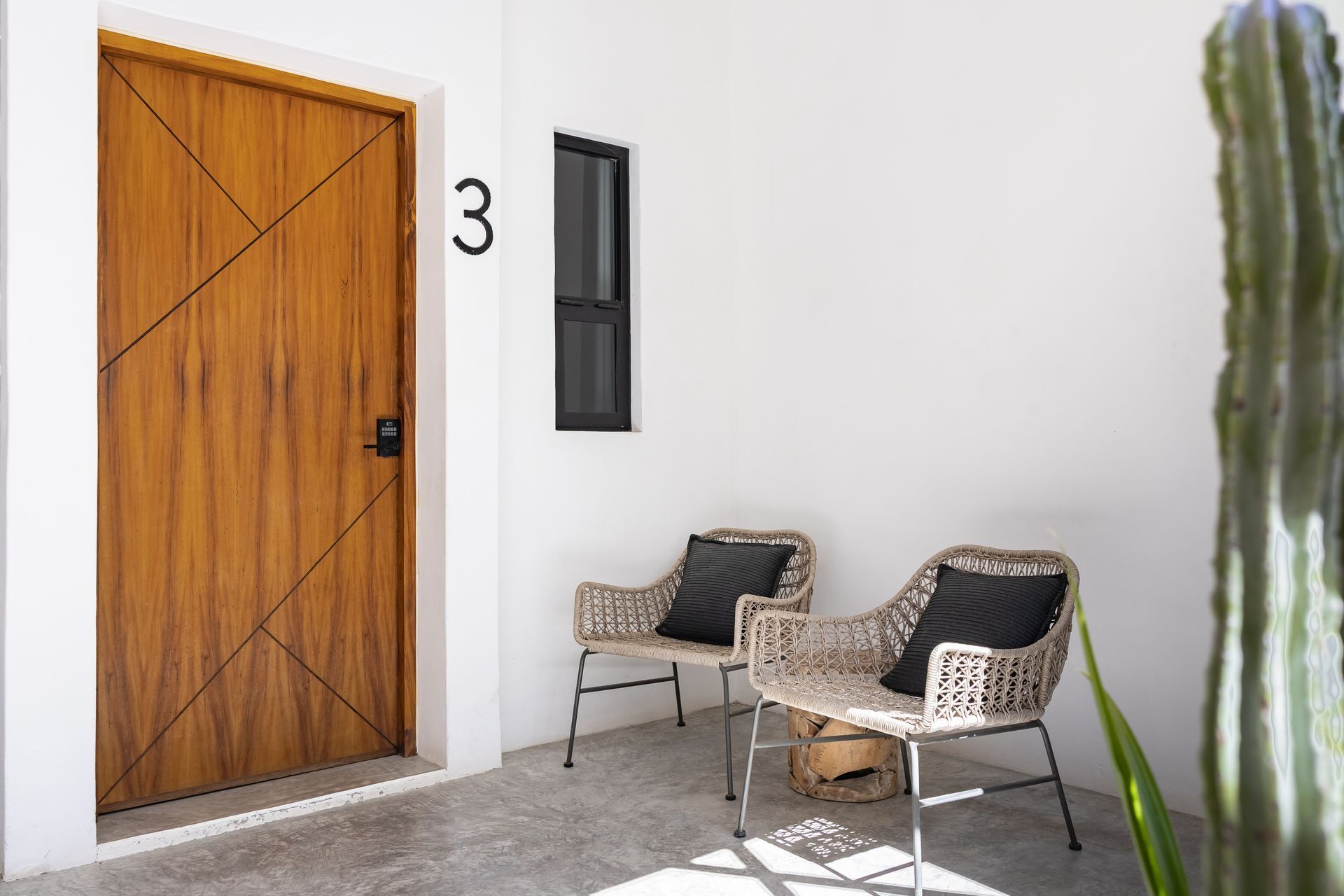 Wooden door with number 3, two wicker chairs with black pillows, and a cactus.