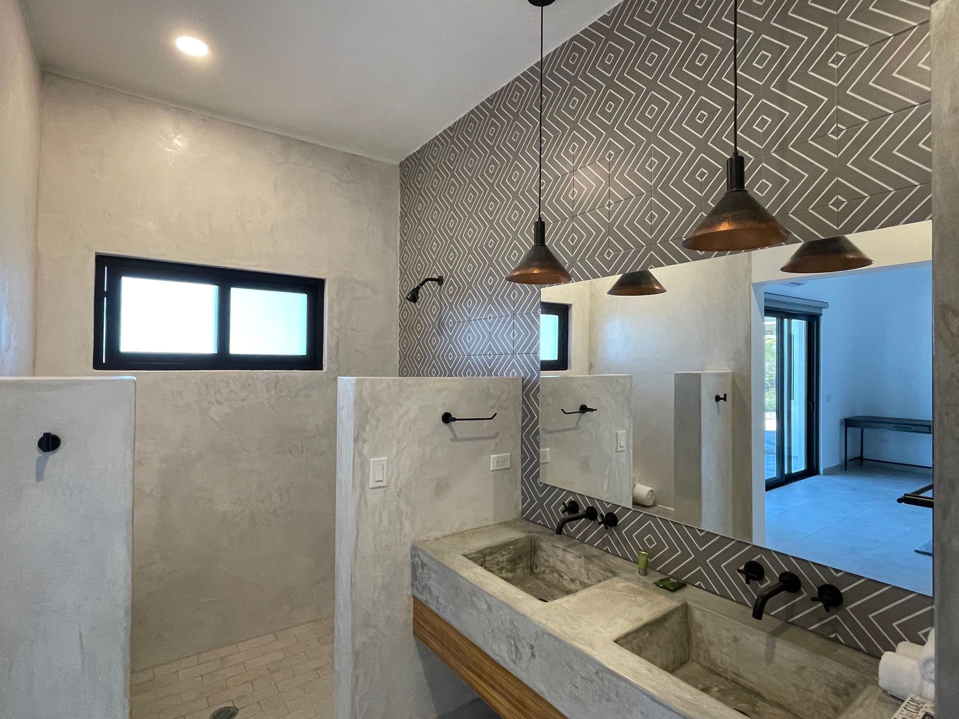 Bathroom with concrete sinks and shower, geometric tile accent wall, pendant lights.