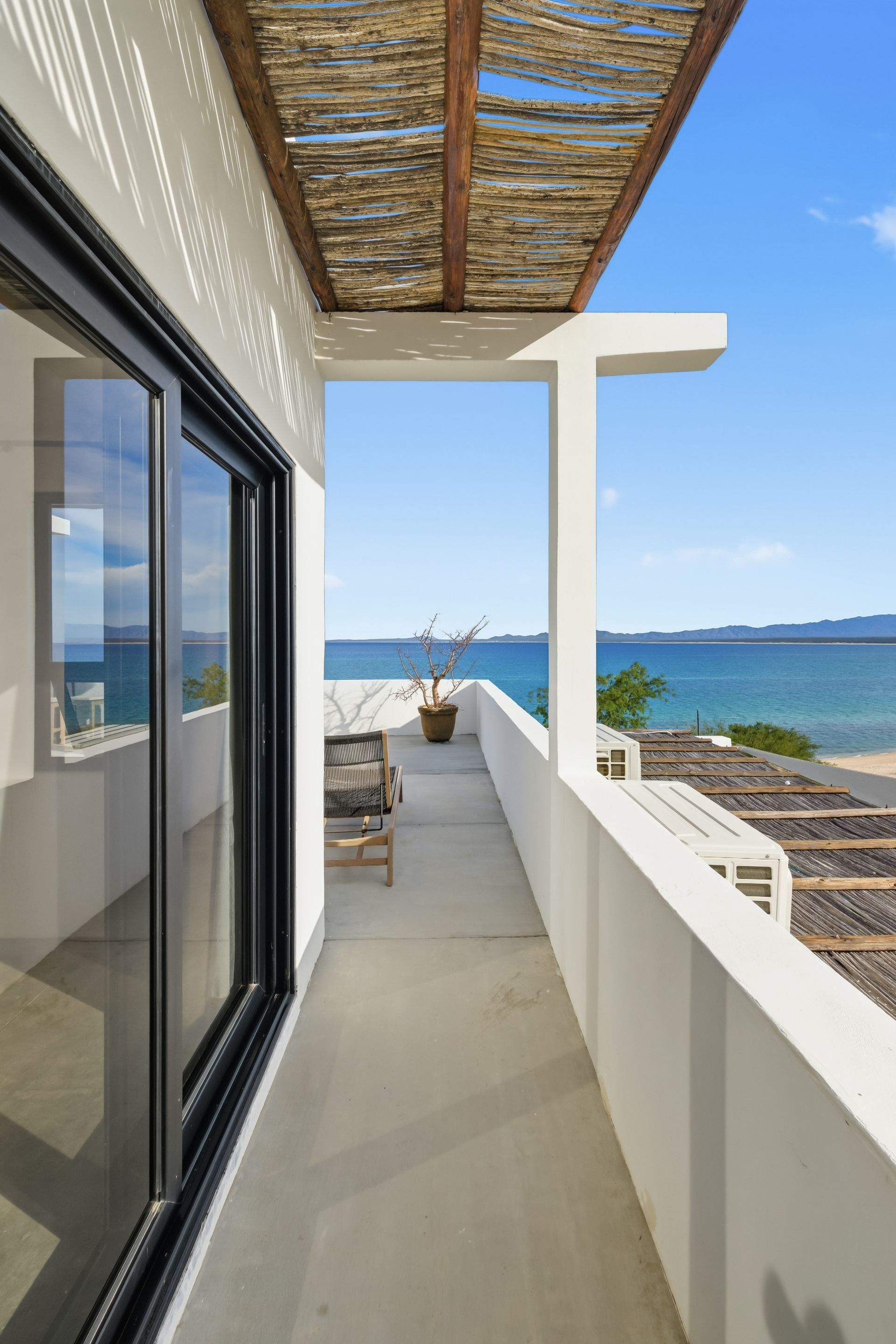 Balcony overlooking ocean; white walls, sliding glass door, woven roof.