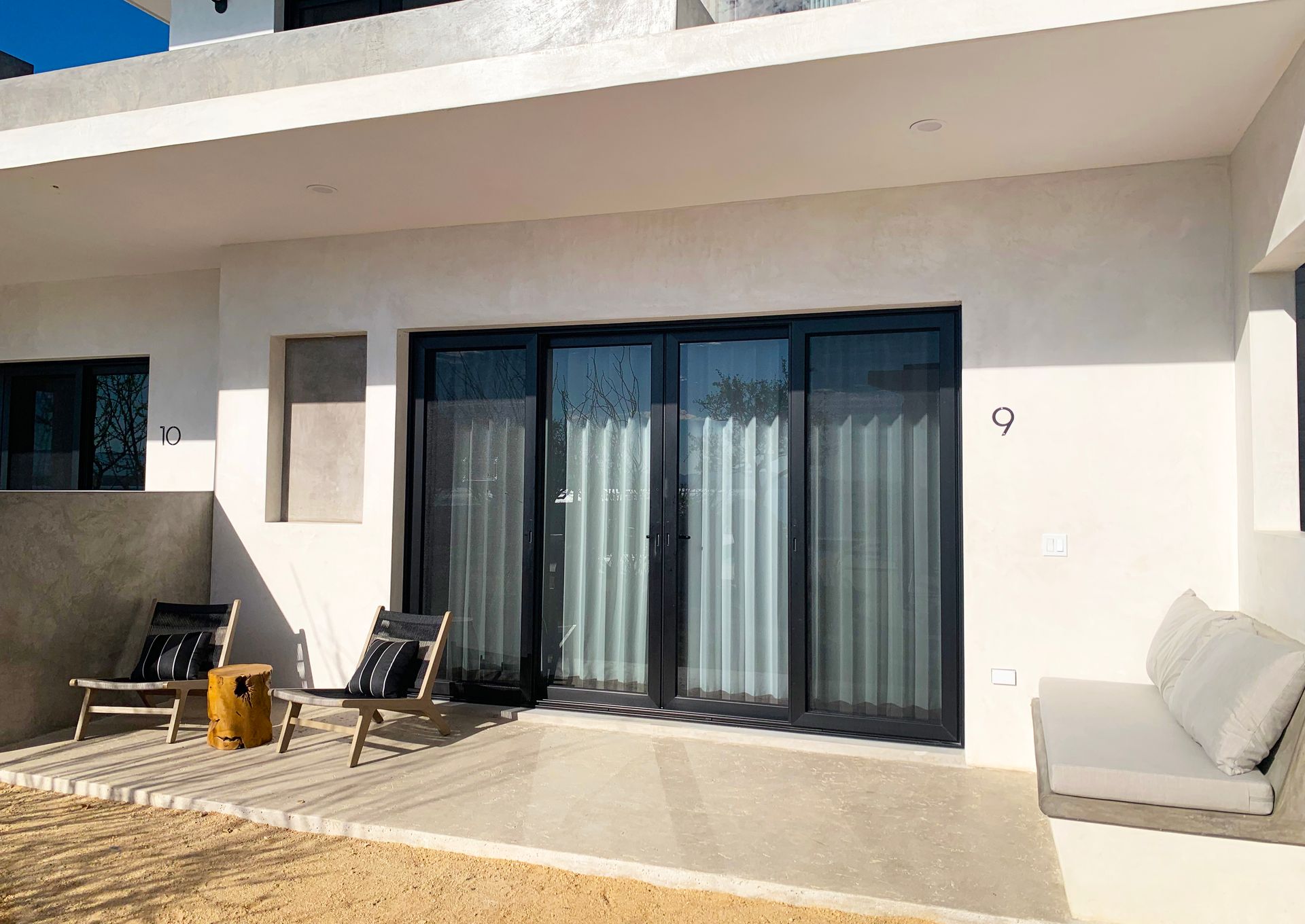 Patio with sliding glass doors, chairs, and a small couch on a sunny day.