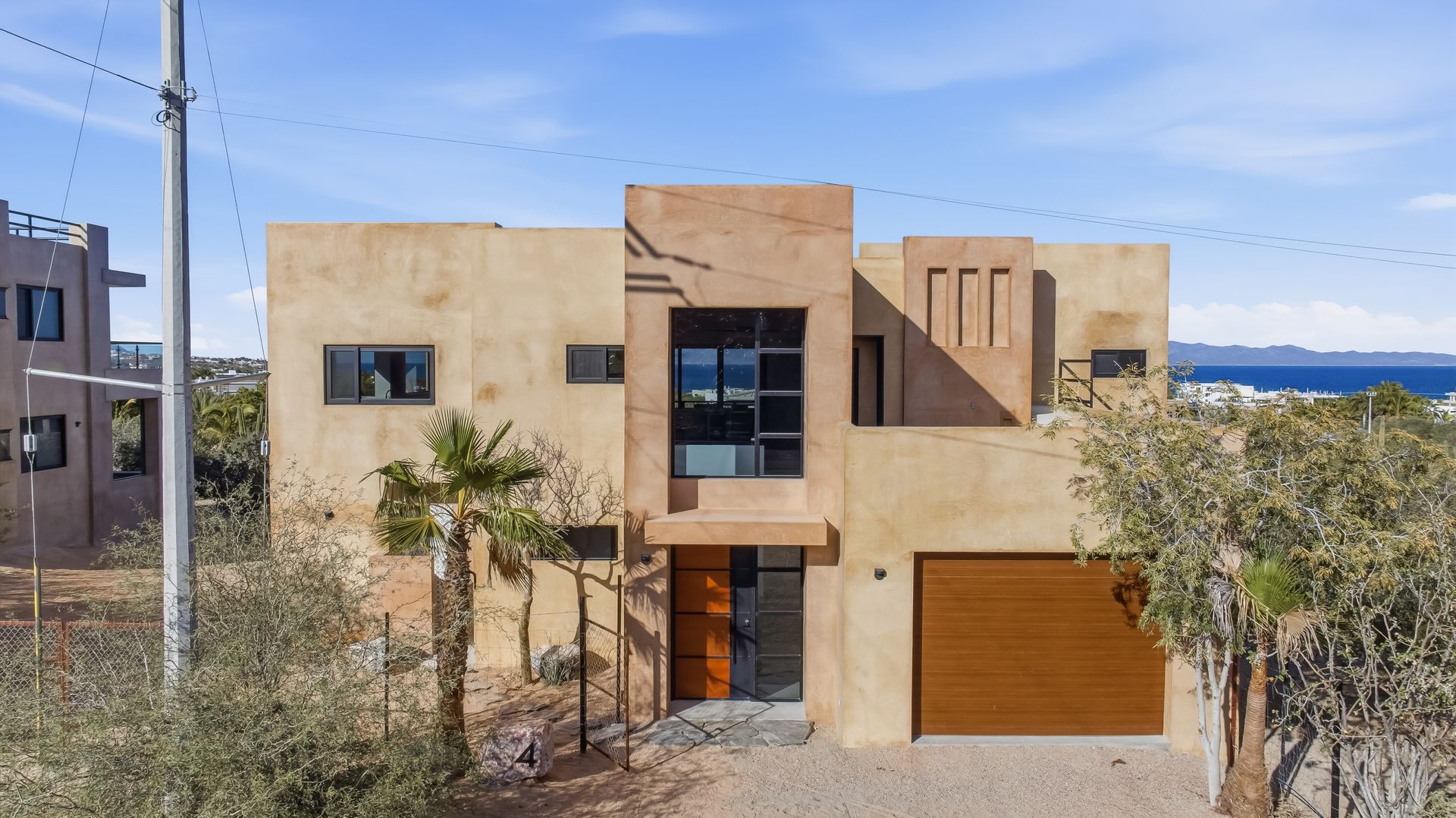 Two-story stucco home with a wooden garage door and dark-framed windows; ocean view.