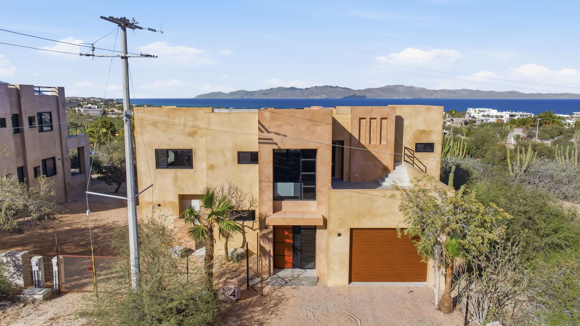 Two-story beige stucco house with a brown garage door, and a view of the ocean.