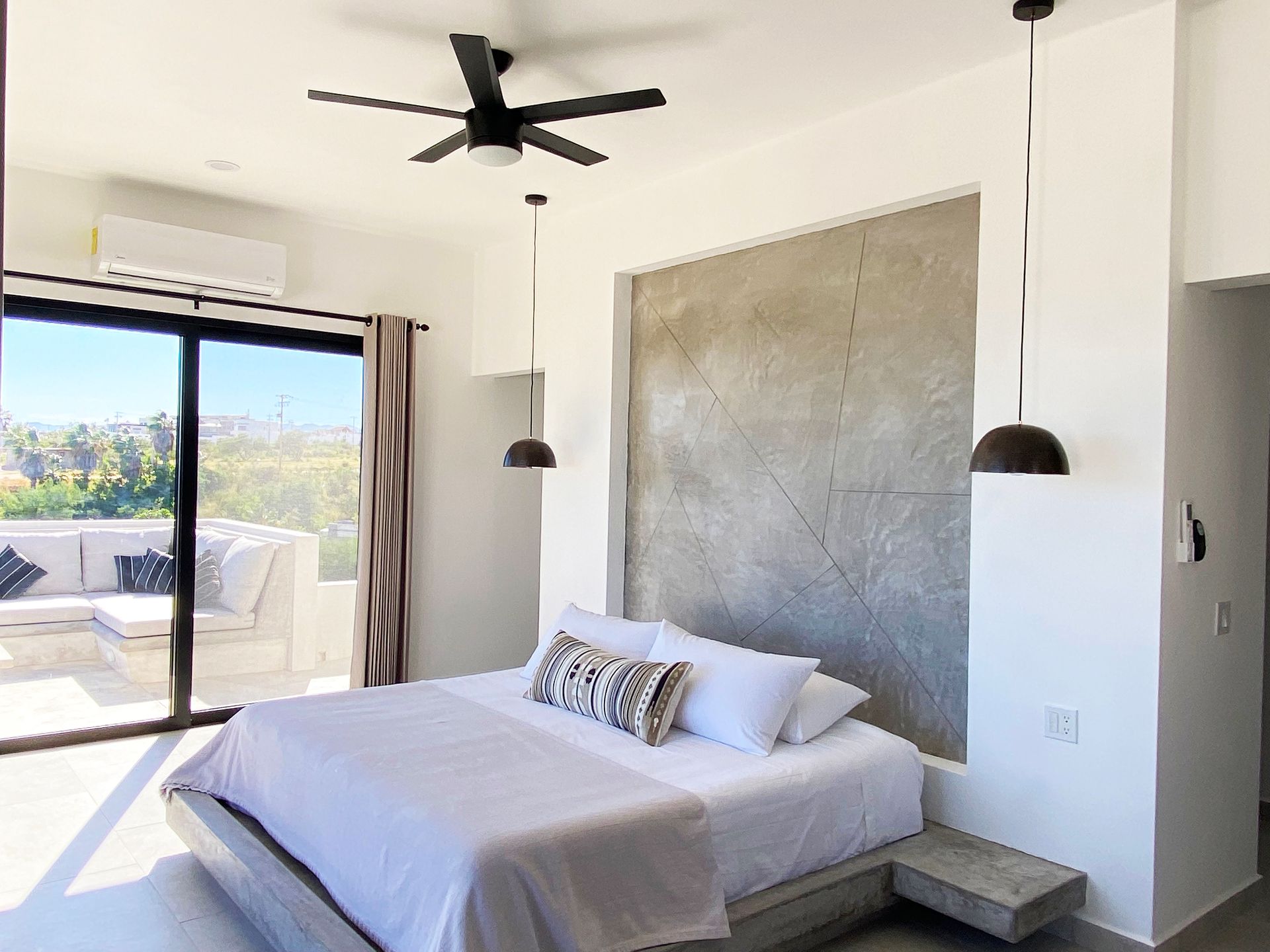 Bedroom with a bed, outdoor balcony, concrete wall, and dark pendant lights.