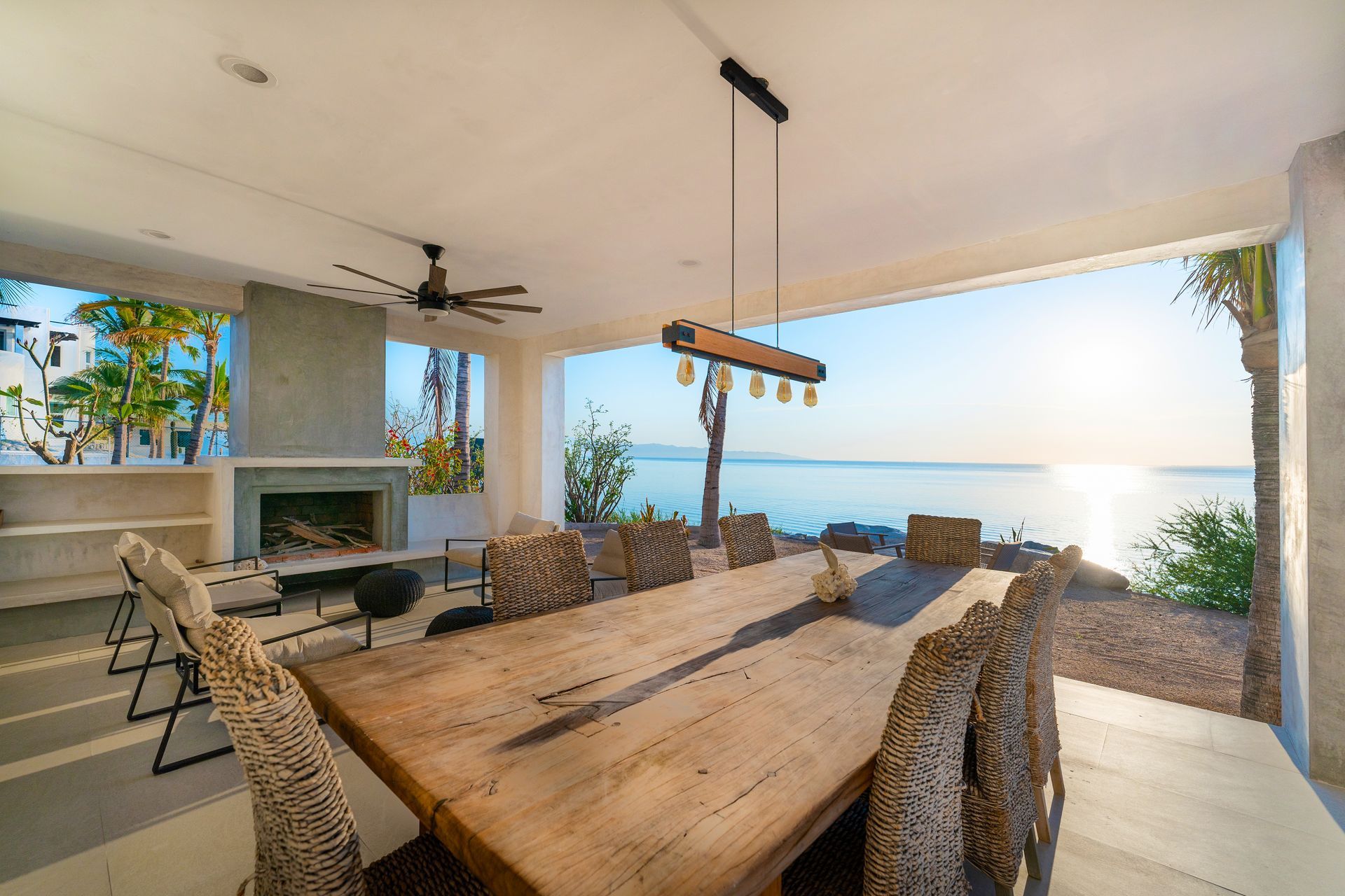Outdoor dining area with a long wooden table, ocean view, and a hanging light fixture.