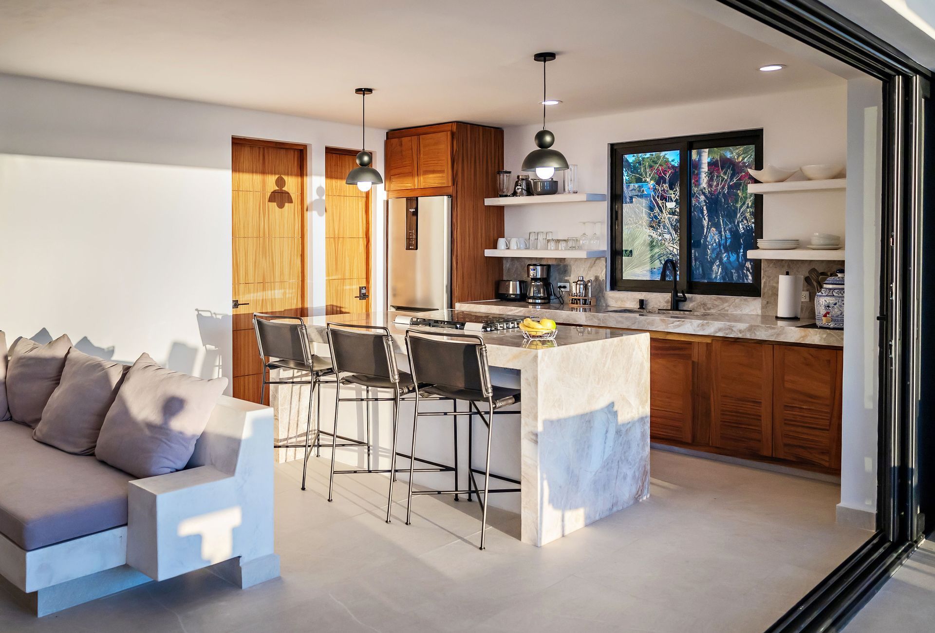 Modern kitchen with island, brown cabinets, open to a living area and outdoor space.