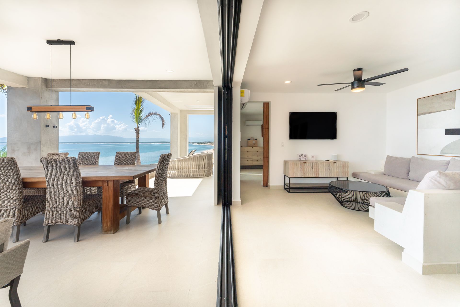 Open-plan living space with dining area overlooking the ocean; living room with sofa, TV, and coffee table.