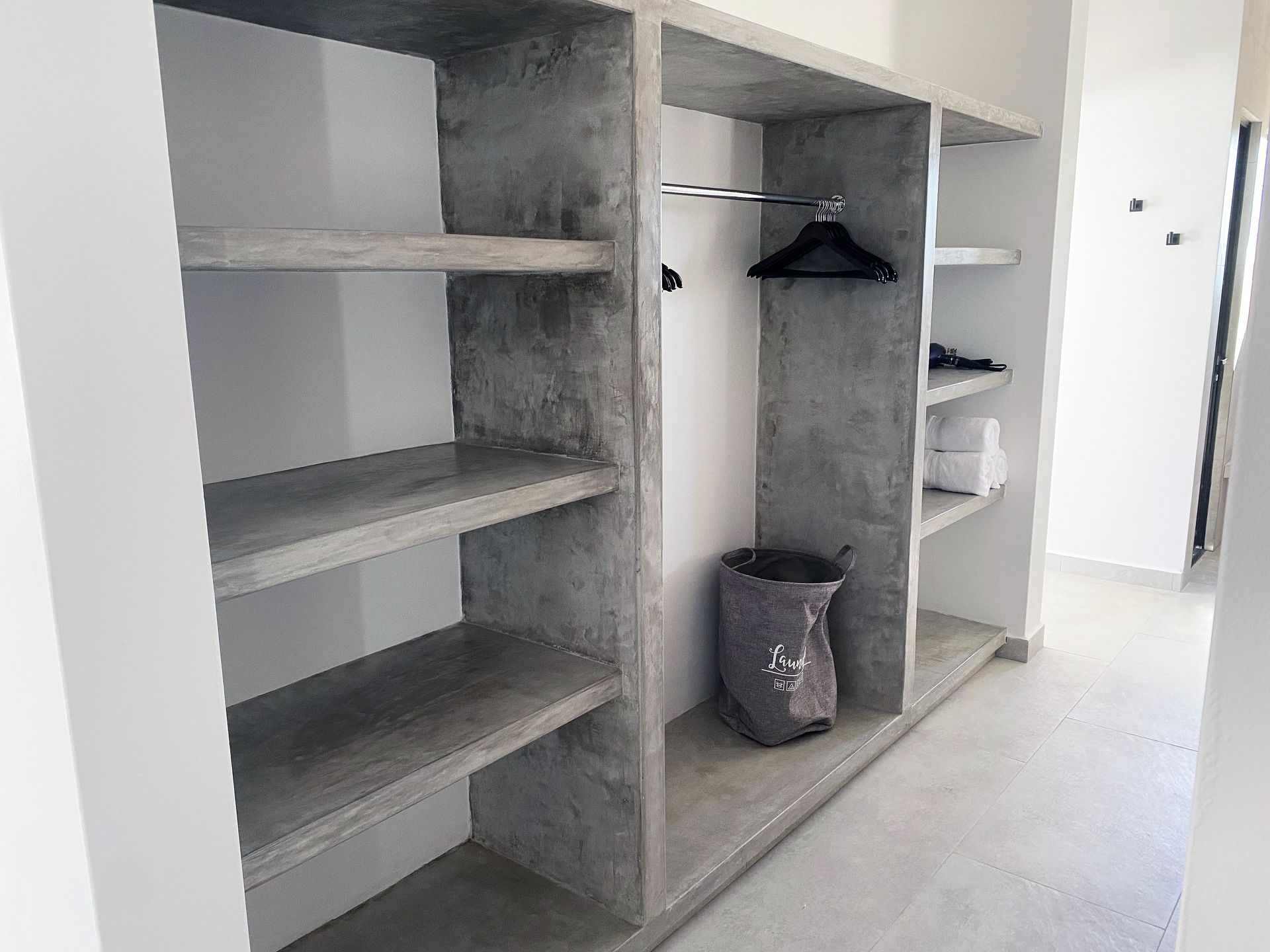 Built-in concrete closet with shelves and hanging rod; a laundry bag is on the floor.