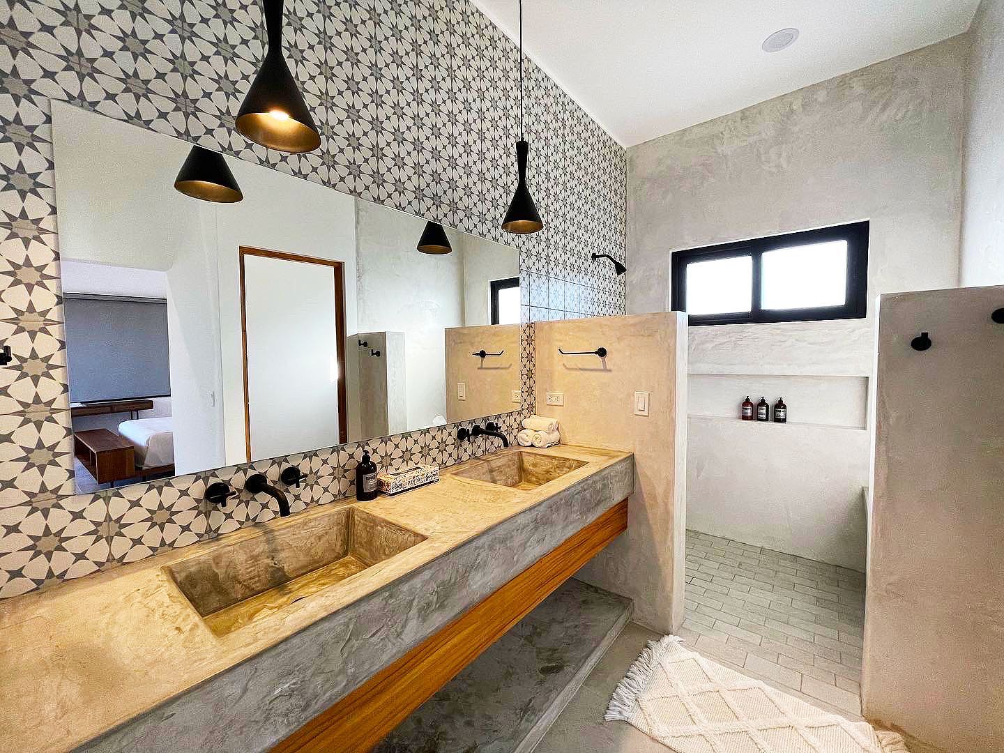 Bathroom with concrete sinks, patterned tile, black fixtures, and pendant lights.
