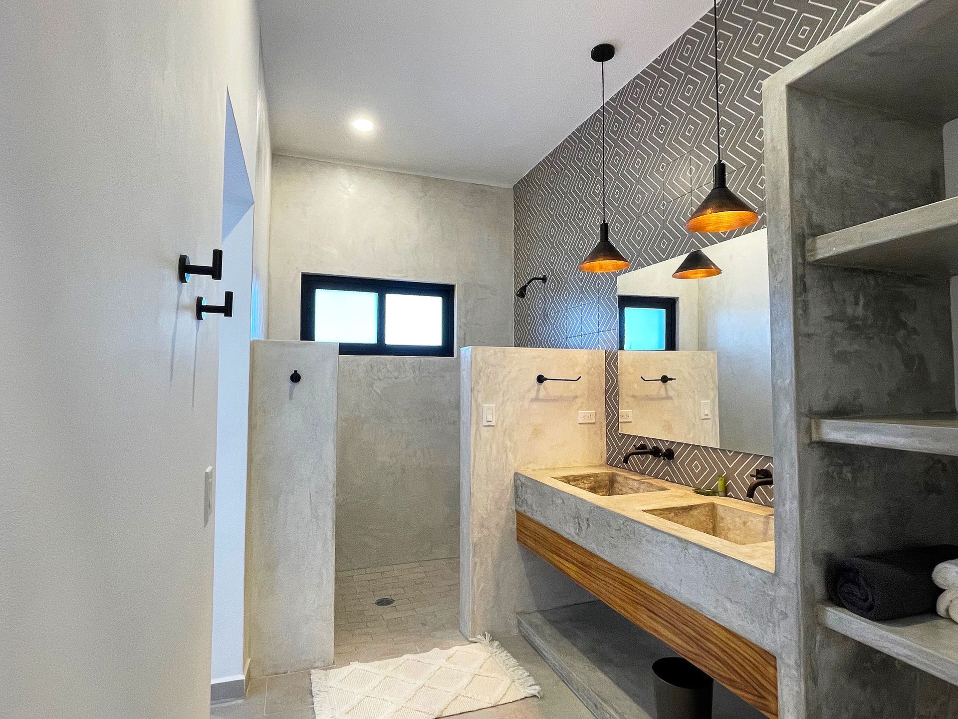 Bathroom with stone walls, double sink, open shower, and black and gold pendant lights.